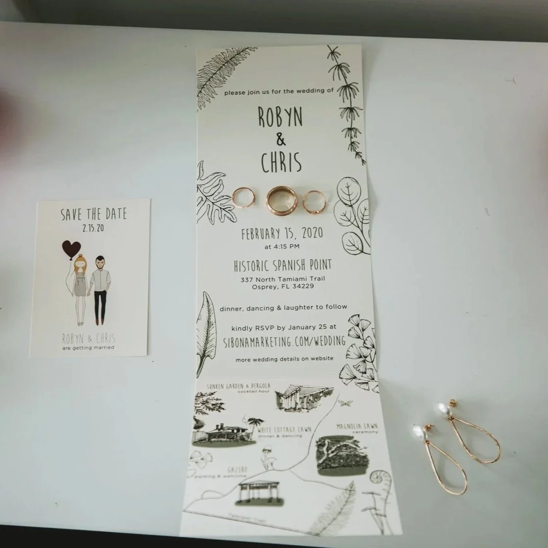 Wedding invitation and save the date card with wedding details, rings, and earrings on a white surface.
