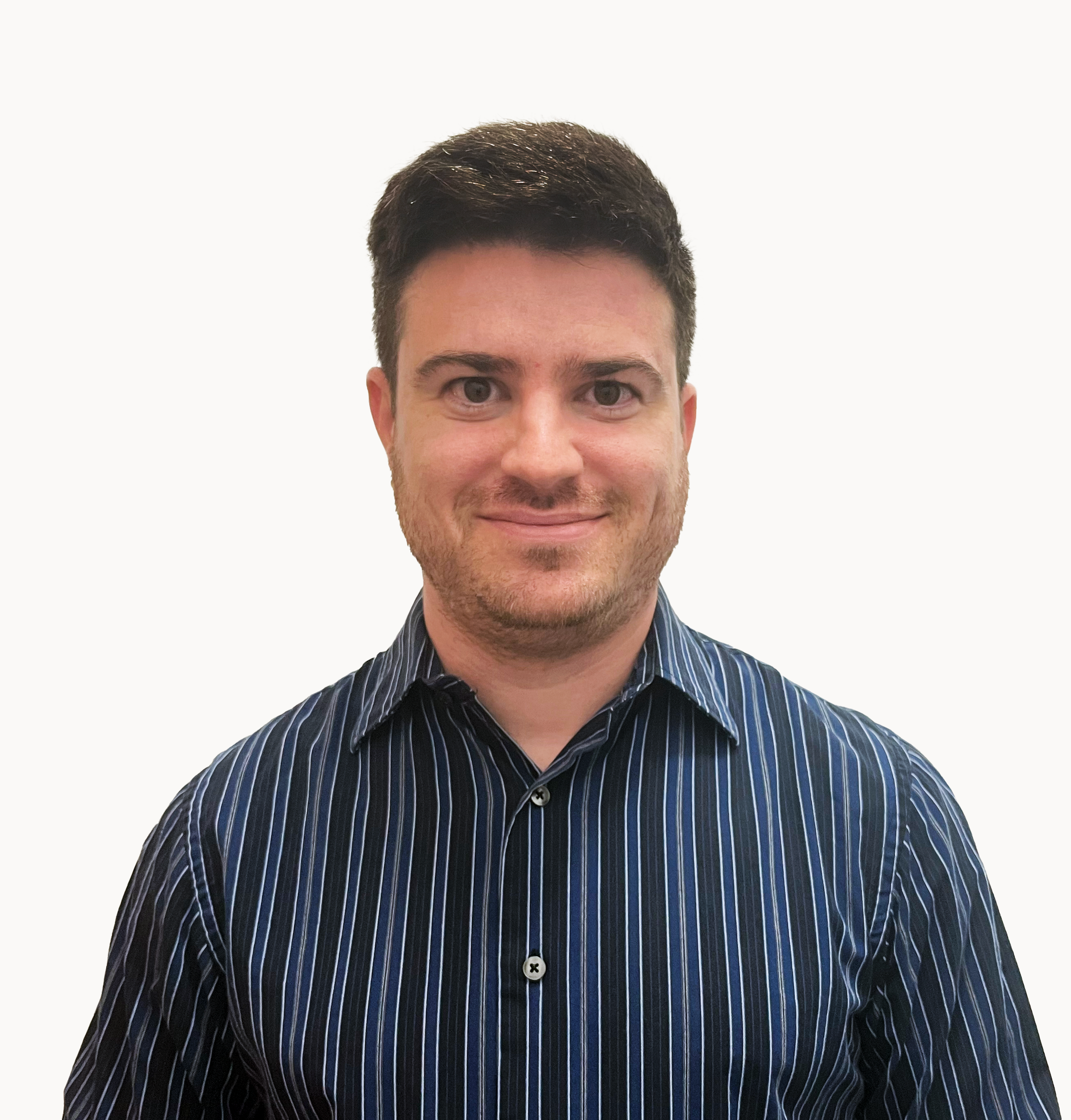 A man with short dark hair, light skin, and a subtle smile, wearing a dark blue striped shirt, stands against a plain white background.