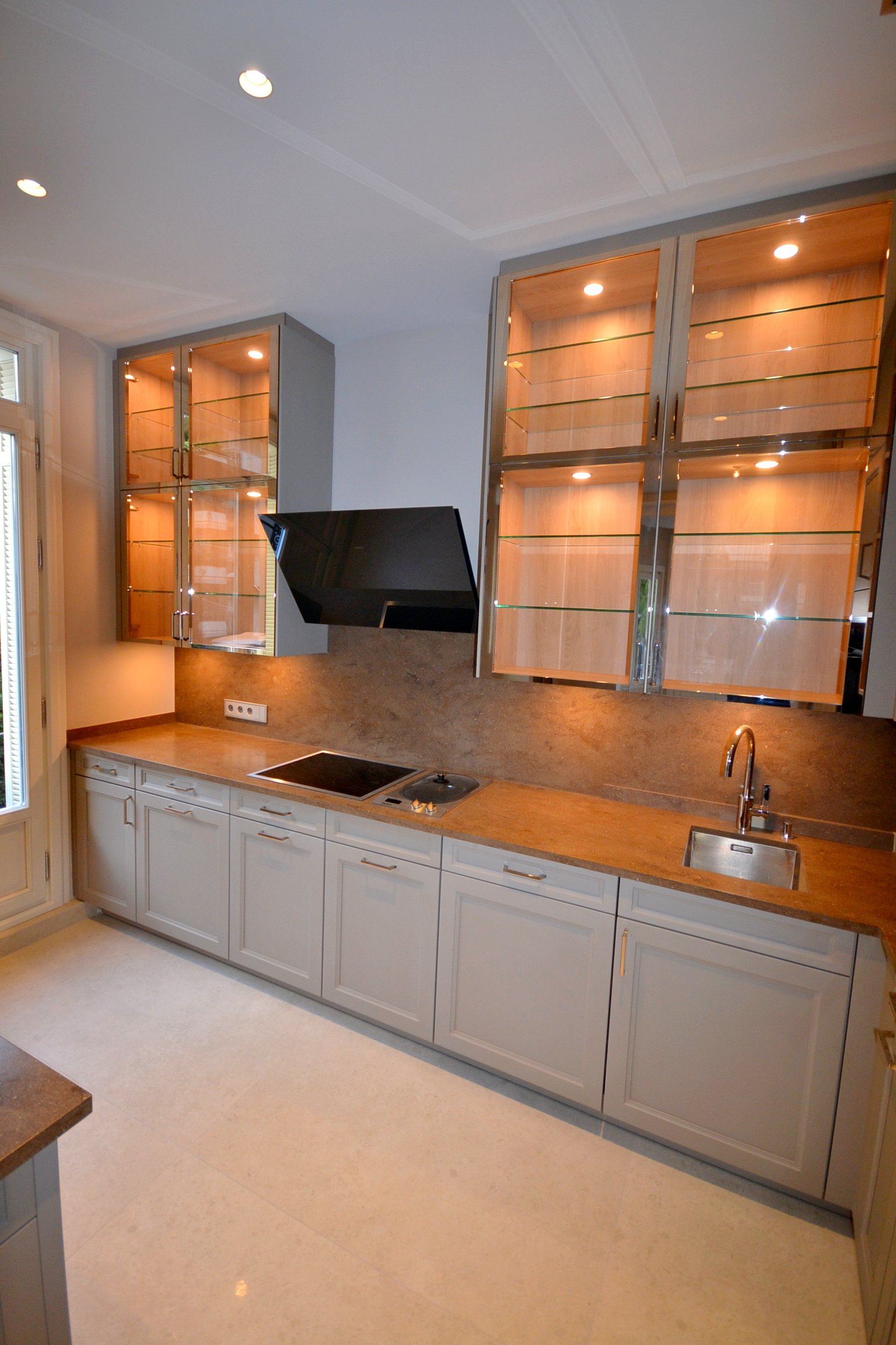 Modern kitchen with gray cabinets, brown countertop, glass-front upper cabinets, a black range hood, and a small stainless steel sink.