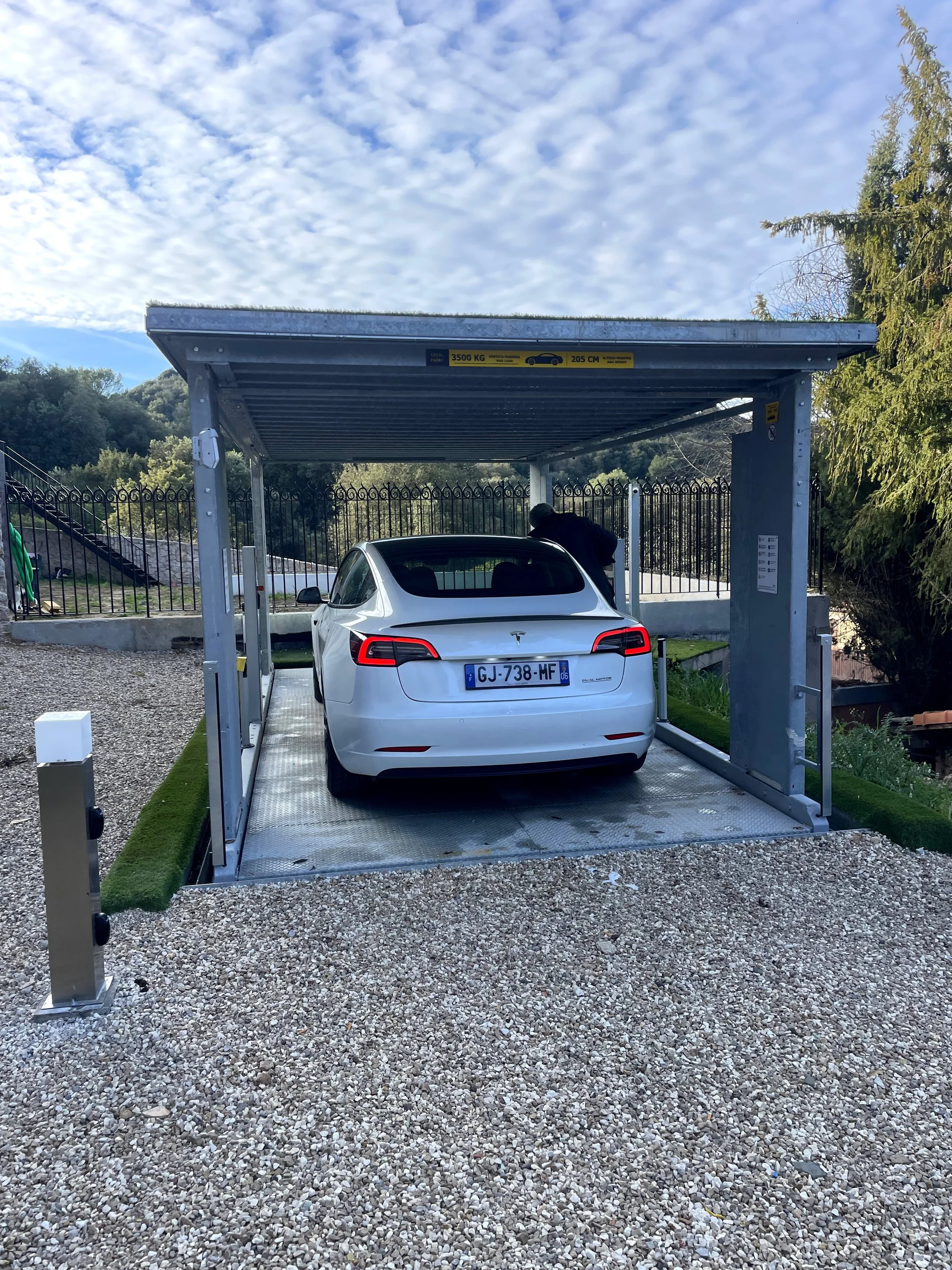 A white Tesla Model 3 parked in an electric vehicle charging station with a metal canopy overhead.