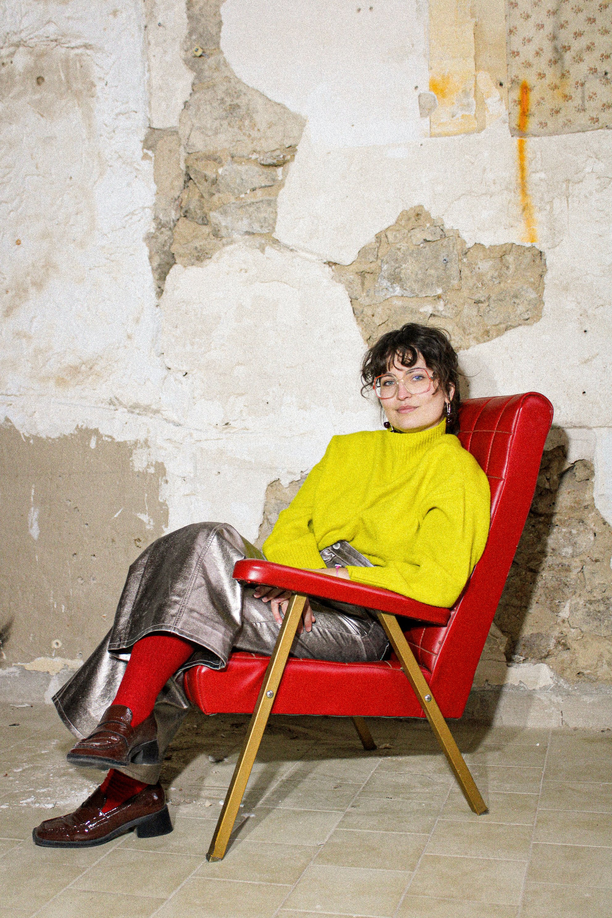 Une femme assise dans un fauteuil rouge avec un mur en pierre en arrière-plan.