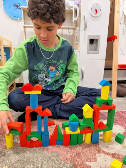 A young boy is sitting on a carpeted floor, playing with colorful building blocks arranged in various structures.