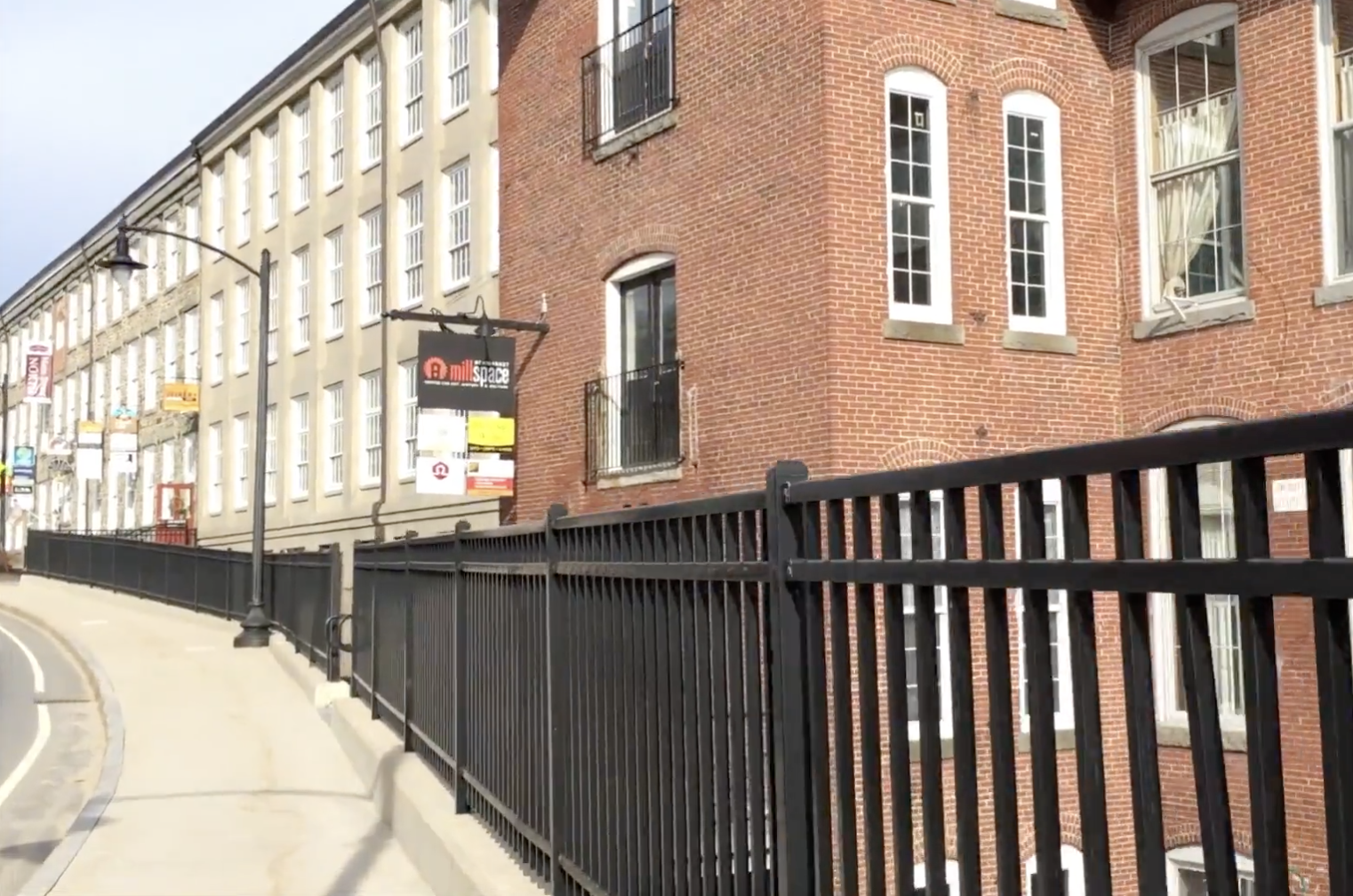 Street view of the Newmarket Millspace showing brick exterior, metal wrought iron fencing, and sidewalk.