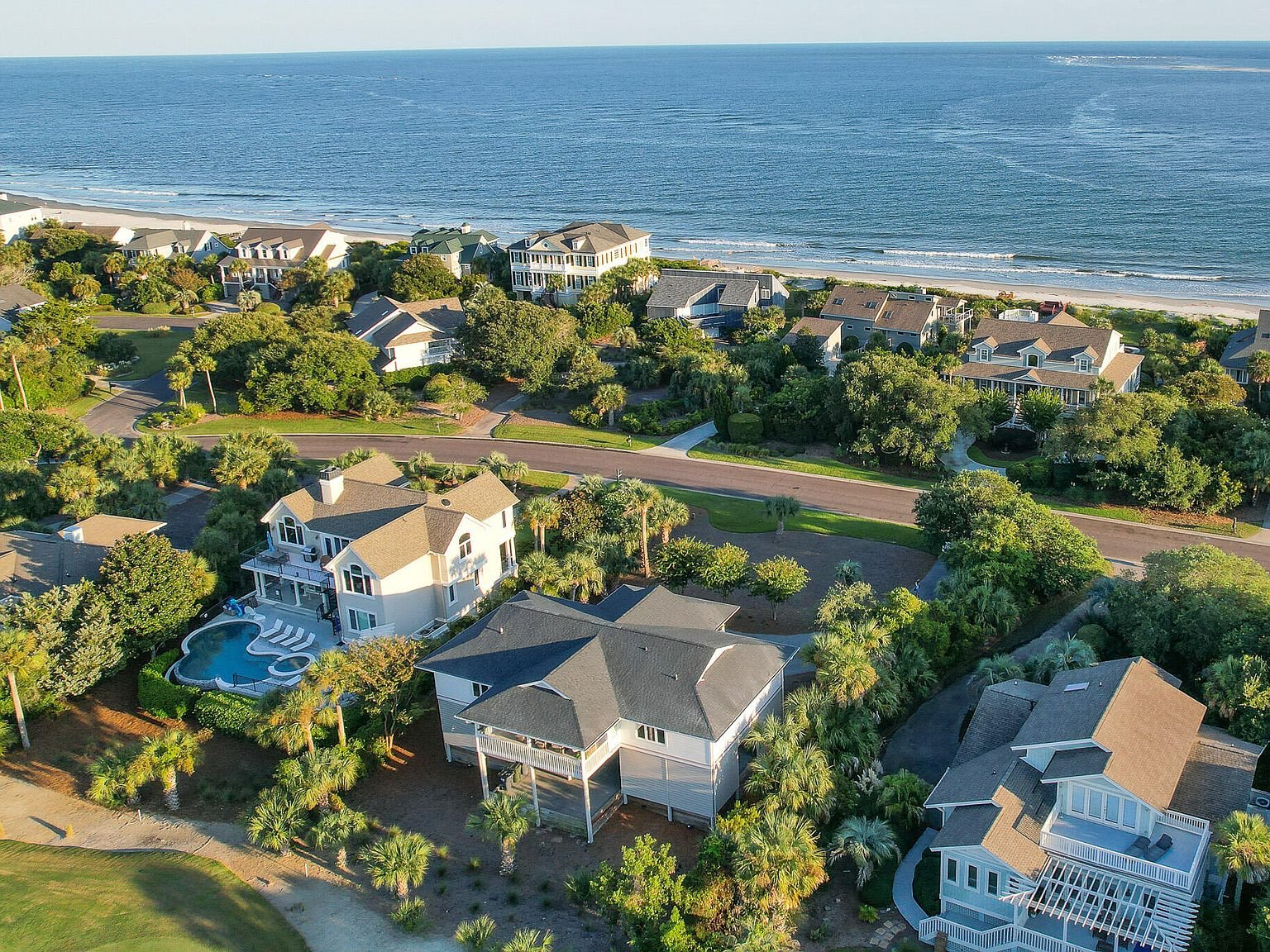 Aerial view of Seabrook Island Club's coastal residential area with houses, roads, trees, and a beach in the background.