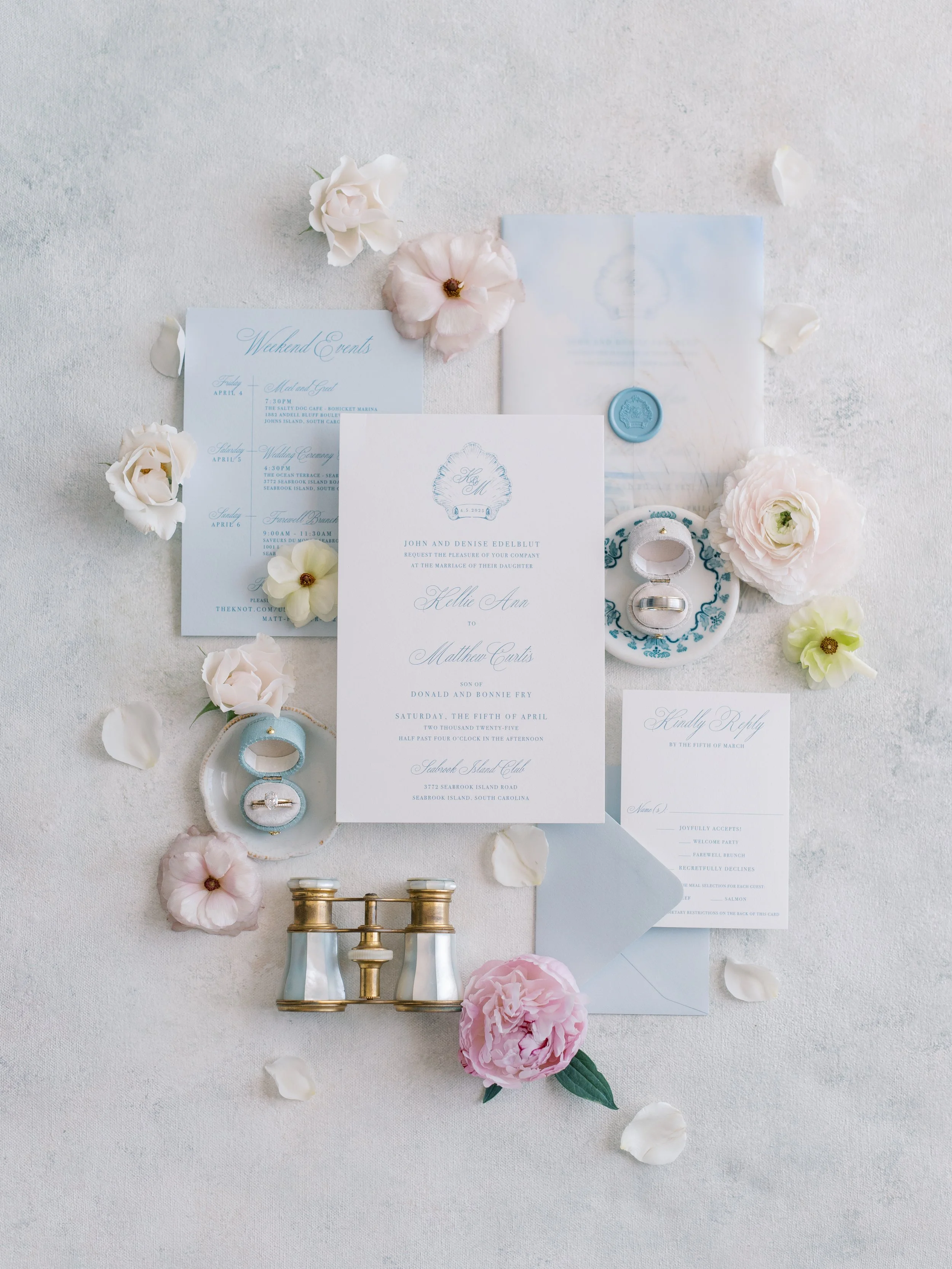 Wedding invitation suite with floral accents, wedding rings, vintage binoculars, and a telescope, arranged on a light-colored surface.