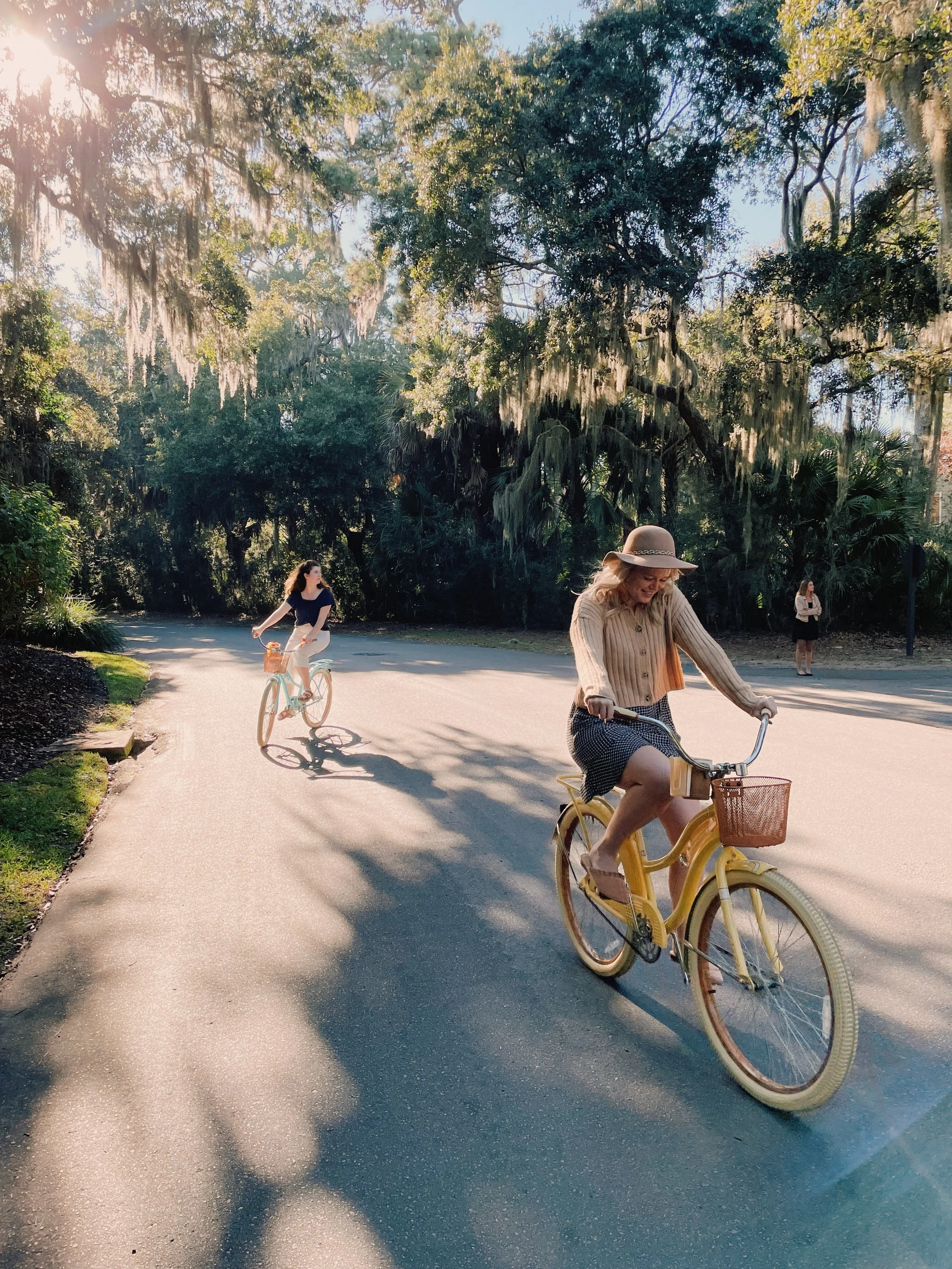 Two women riding bicycles on a tree-lined path during daylight on Seabrook Island.