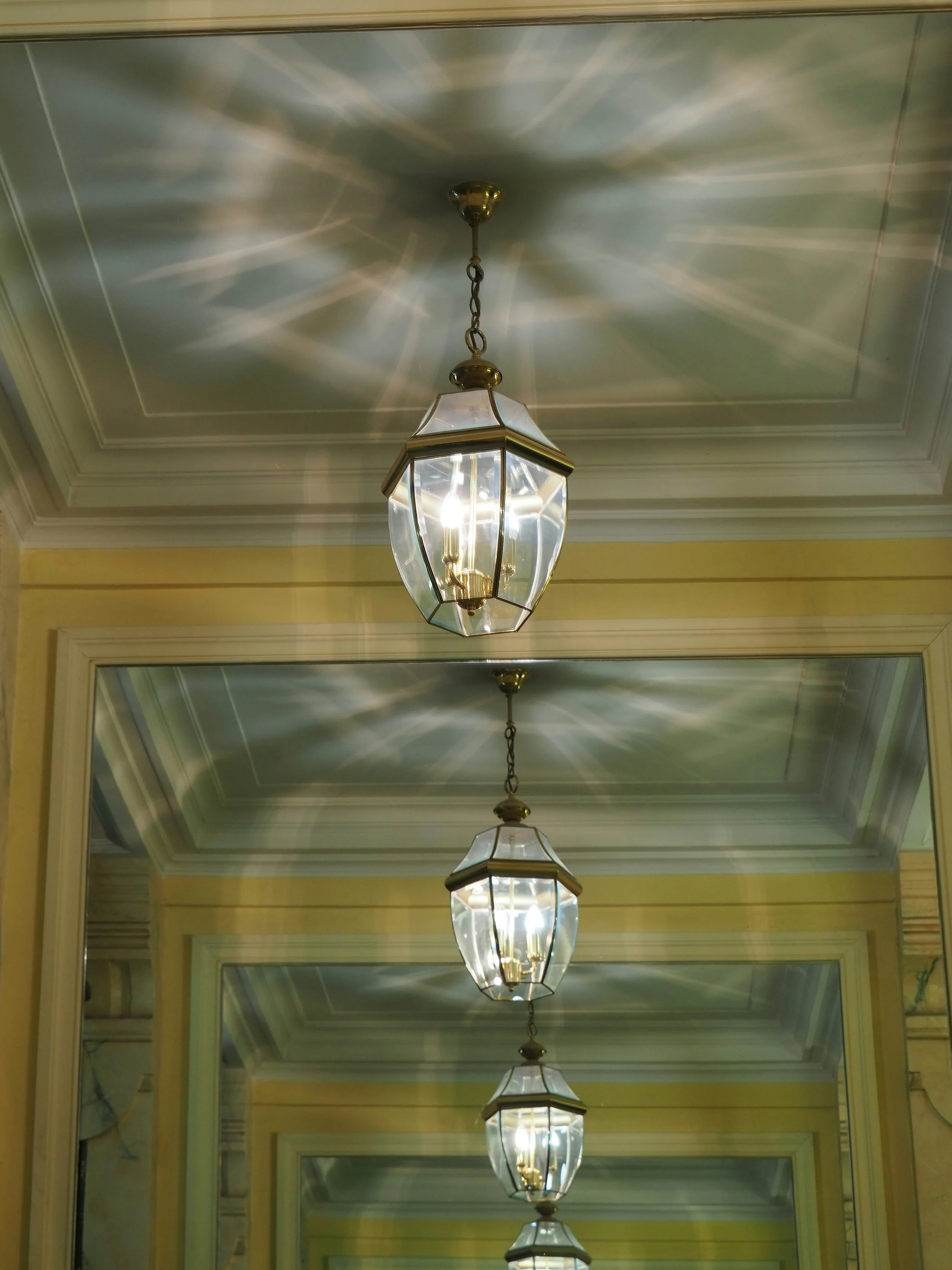 Multiple hanging light fixtures on a ceiling, casting reflections on a mirror below.