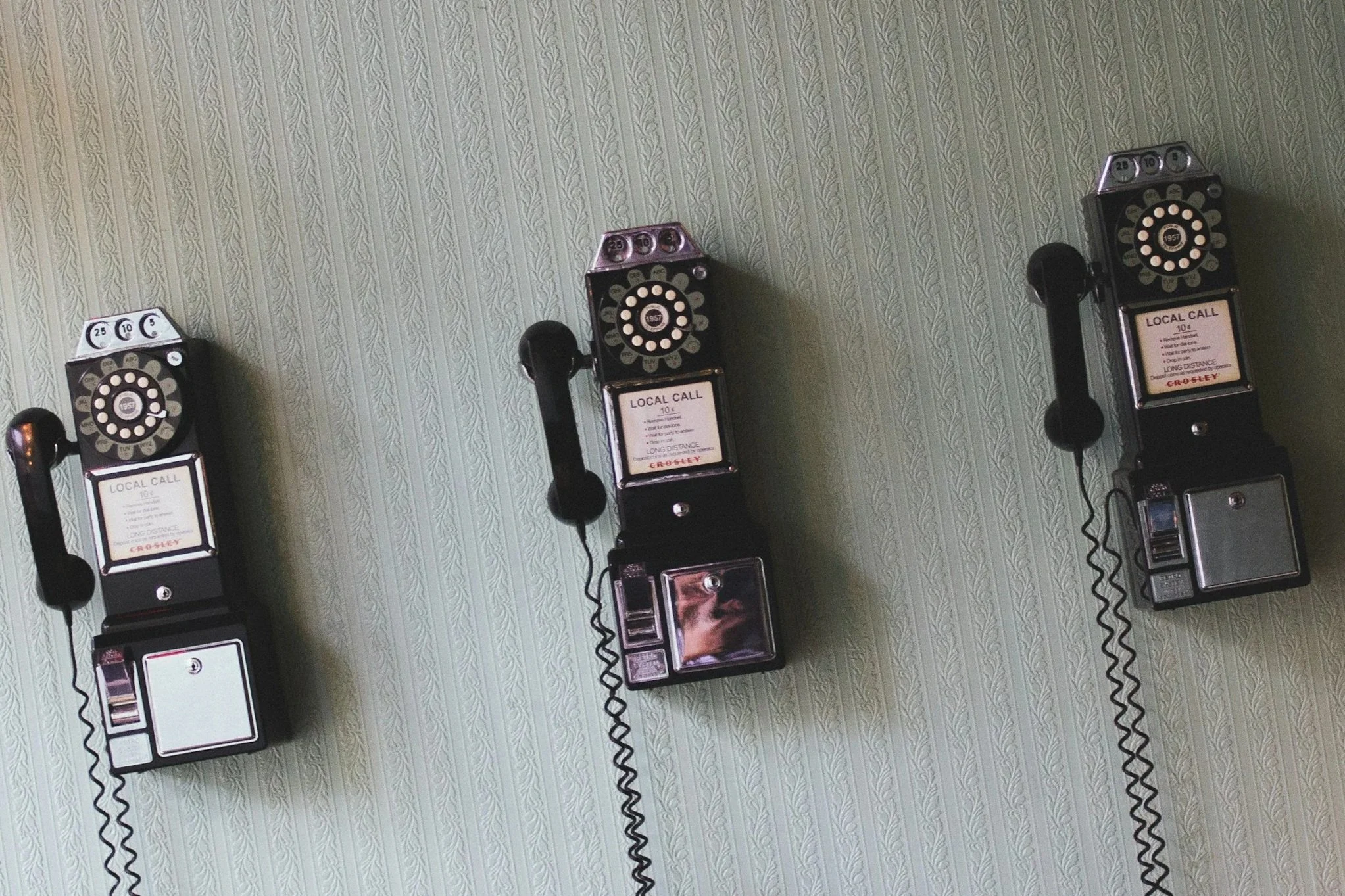 A wall with a textured, striped wallpaper featuring a row of vintage rotary payphones mounted on the wall.