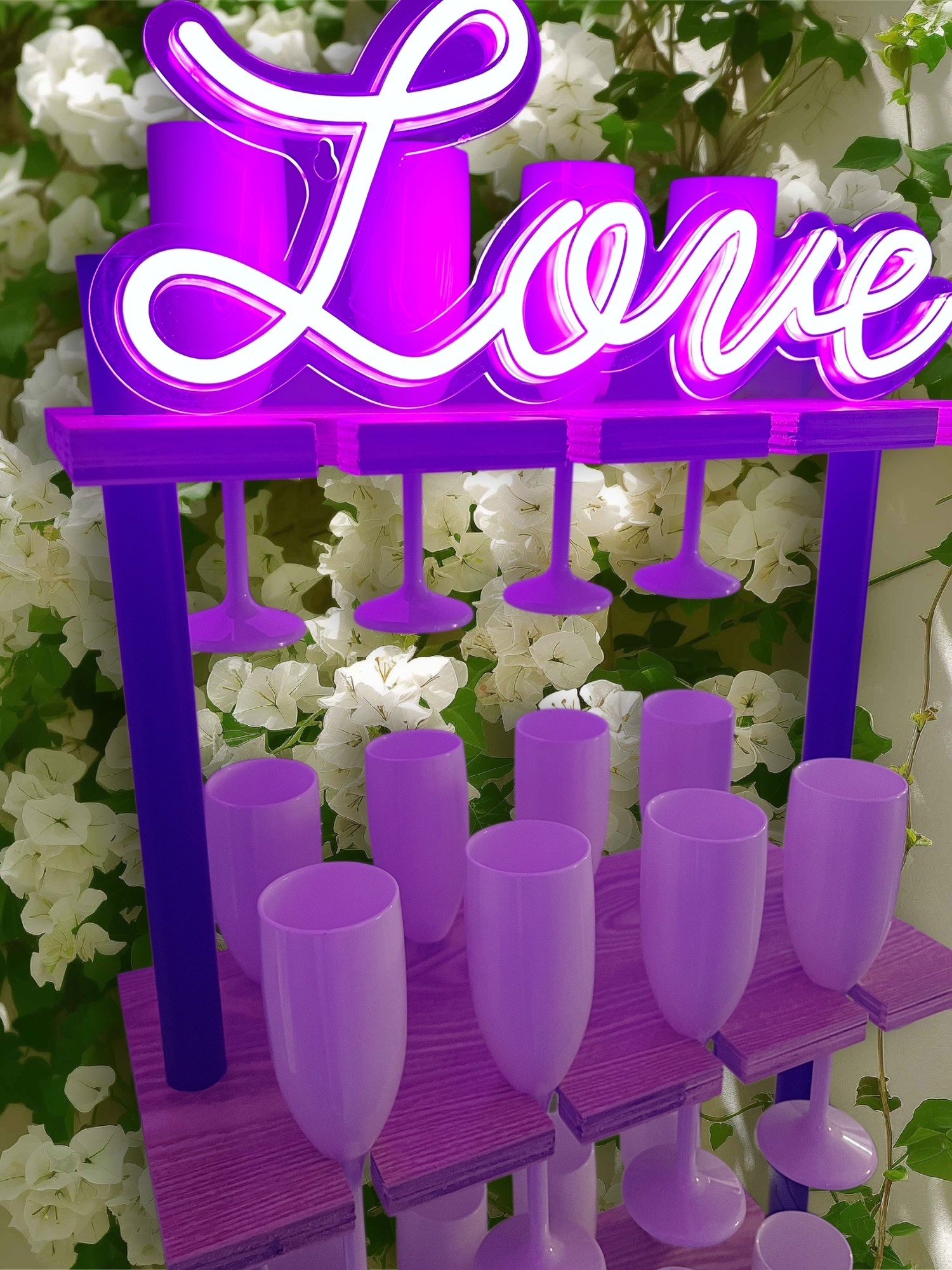 Neon sign that says 'Love' in cursive, illuminated in purple and white, with a backdrop of white flowers and greenery.