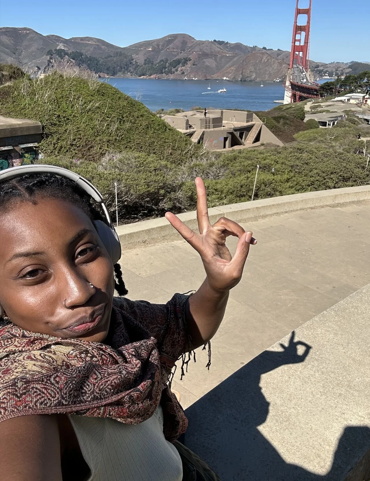 A woman taking a selfie with the Golden Gate Bridge in San Francisco in the background on a sunny day.