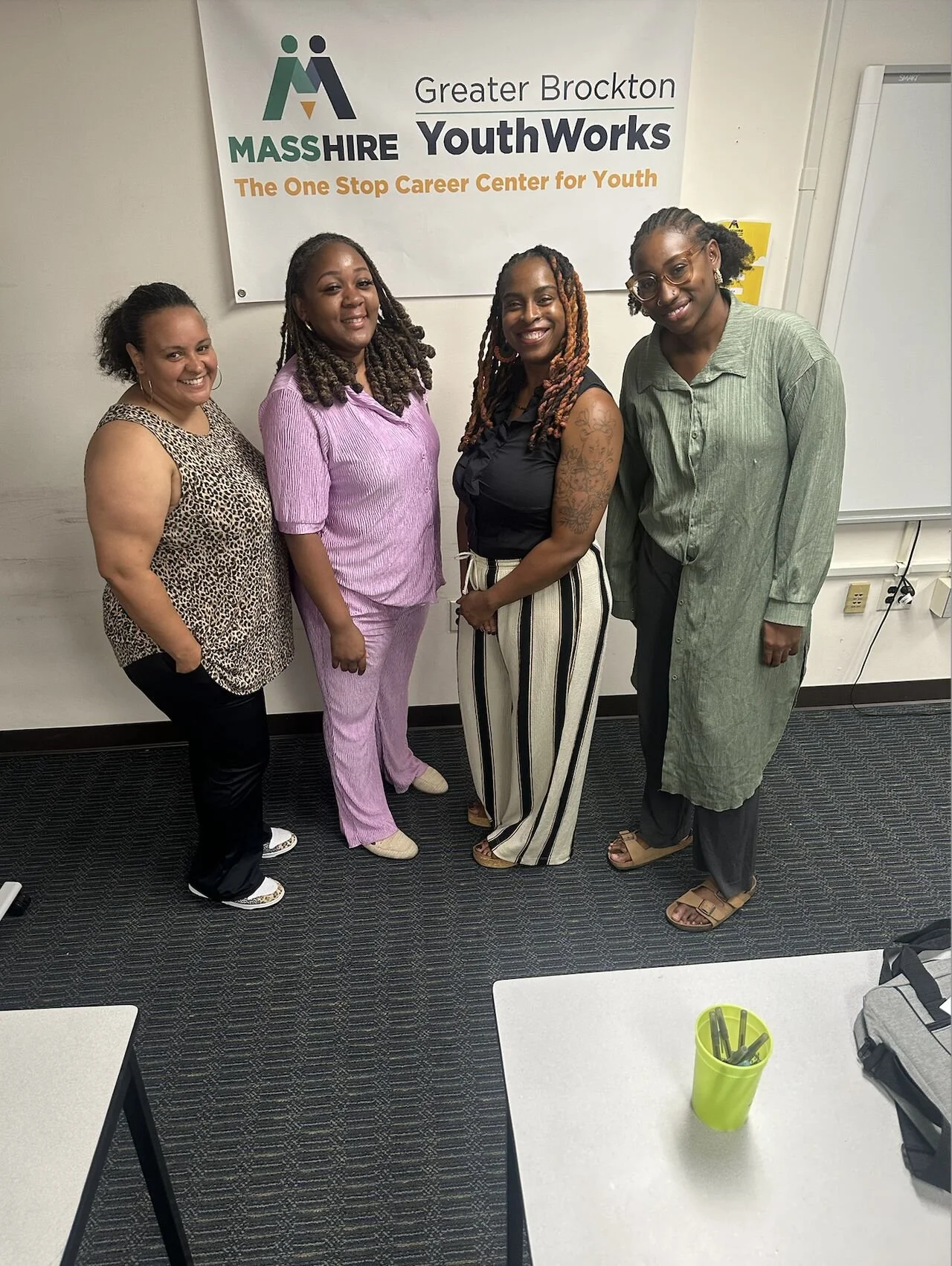 Four women standing together in front of a sign that reads 'Greater Brockton MASS HIRE YouthWorks, The One Stop Career Center for Youth.'