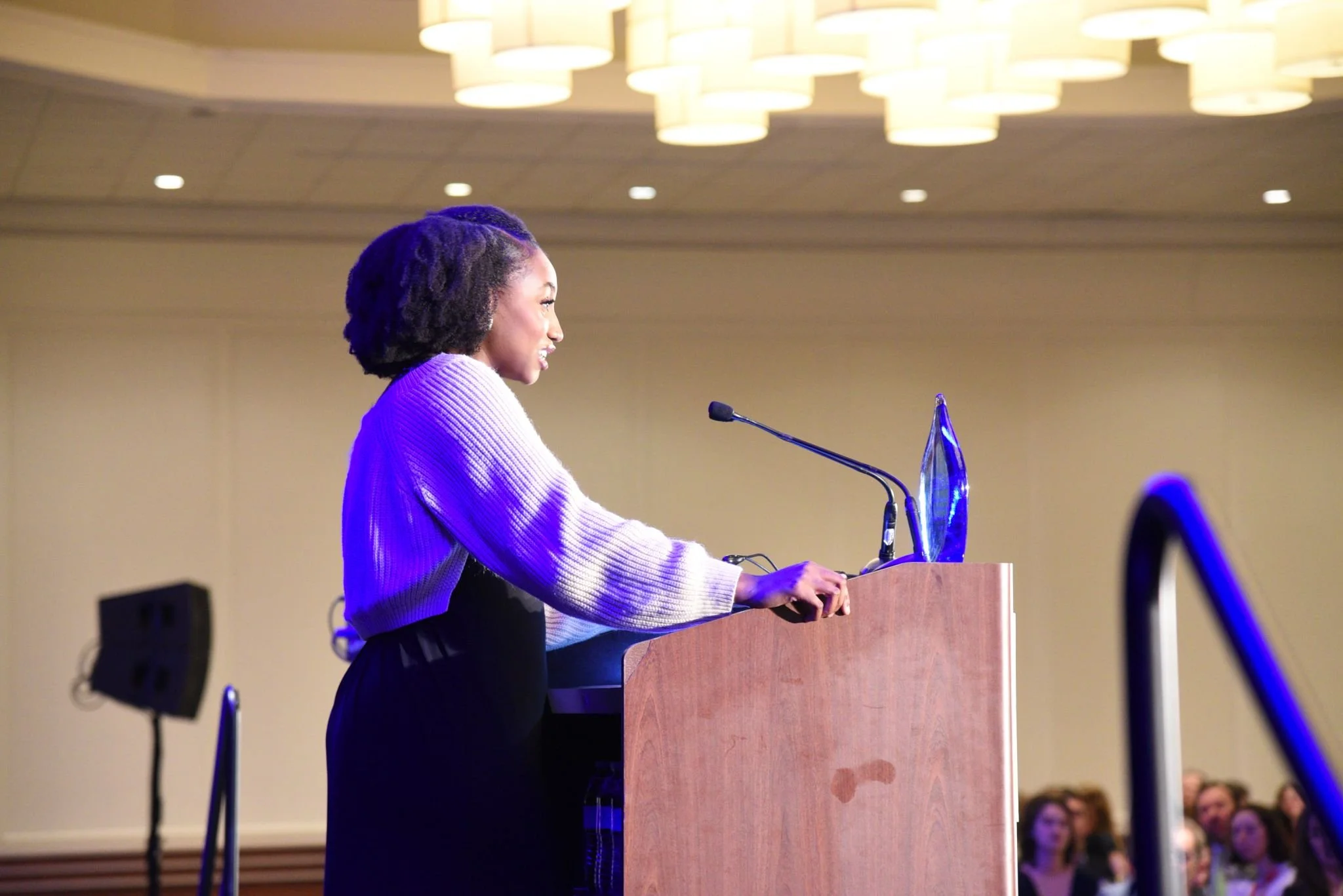 A woman standing at a podium speaking into a microphone during a conference or event.