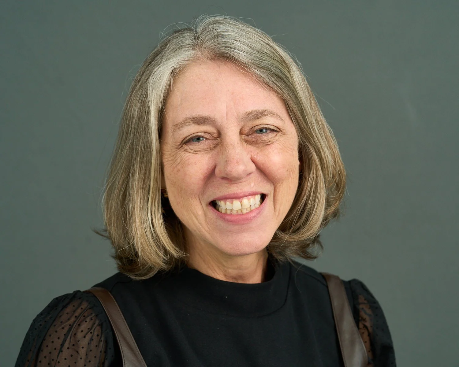 A woman is smiling and wearing a black blouse.