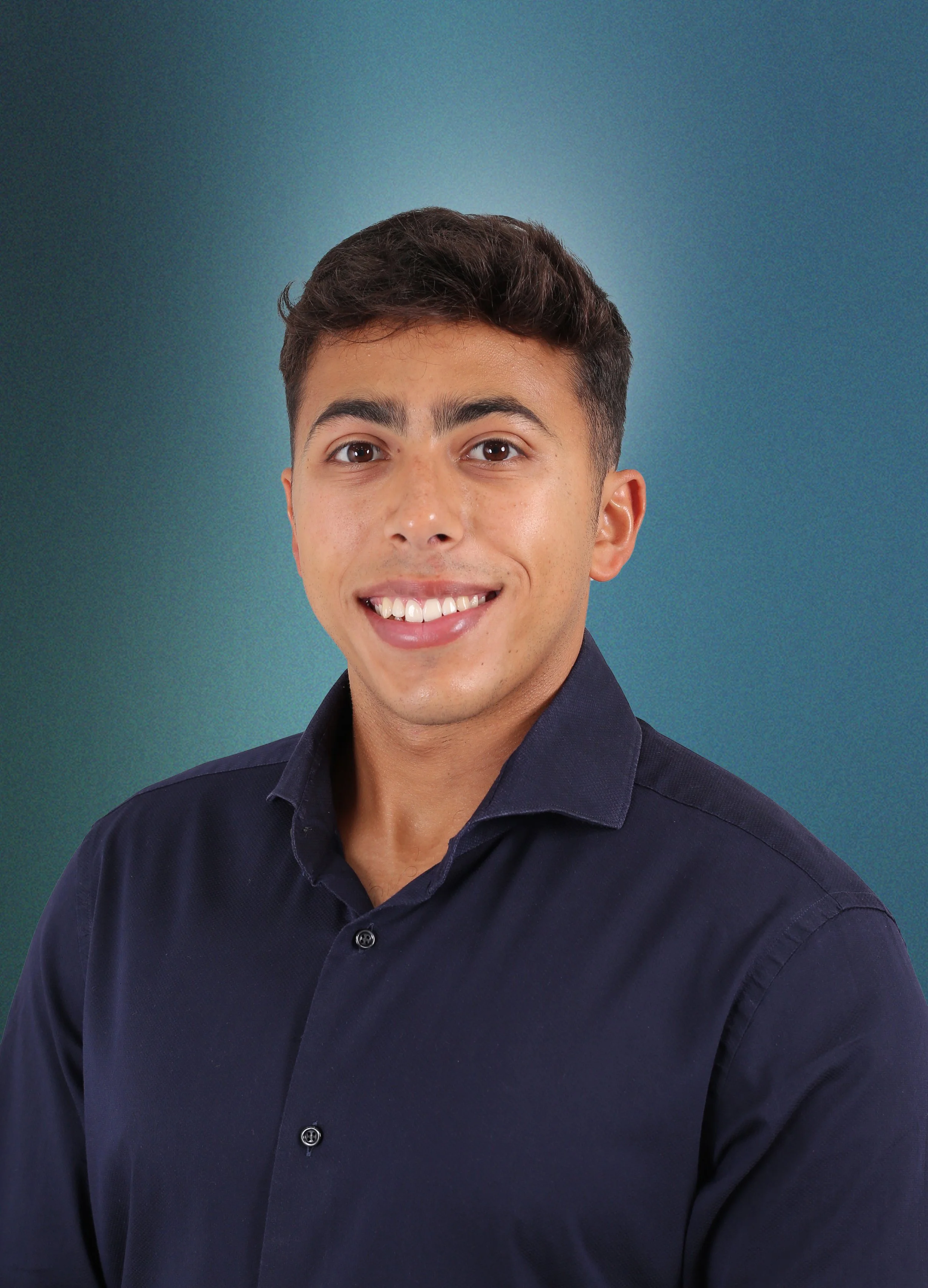 Portrait of a young man with short dark hair, smiling, wearing a navy blue button-up shirt against a gradient teal background.