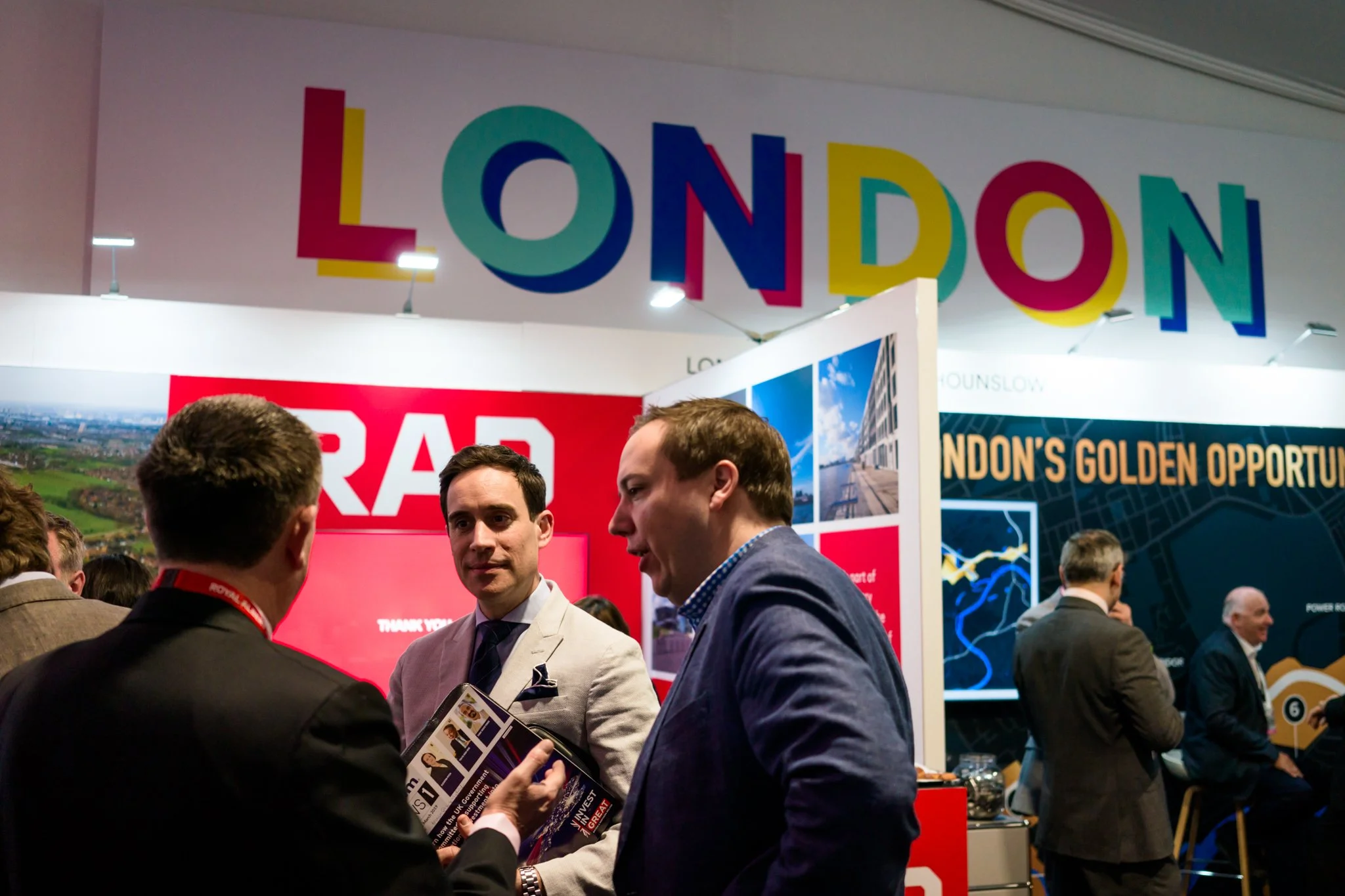 People chatting at a London exhibition booth with colorful London sign overhead.