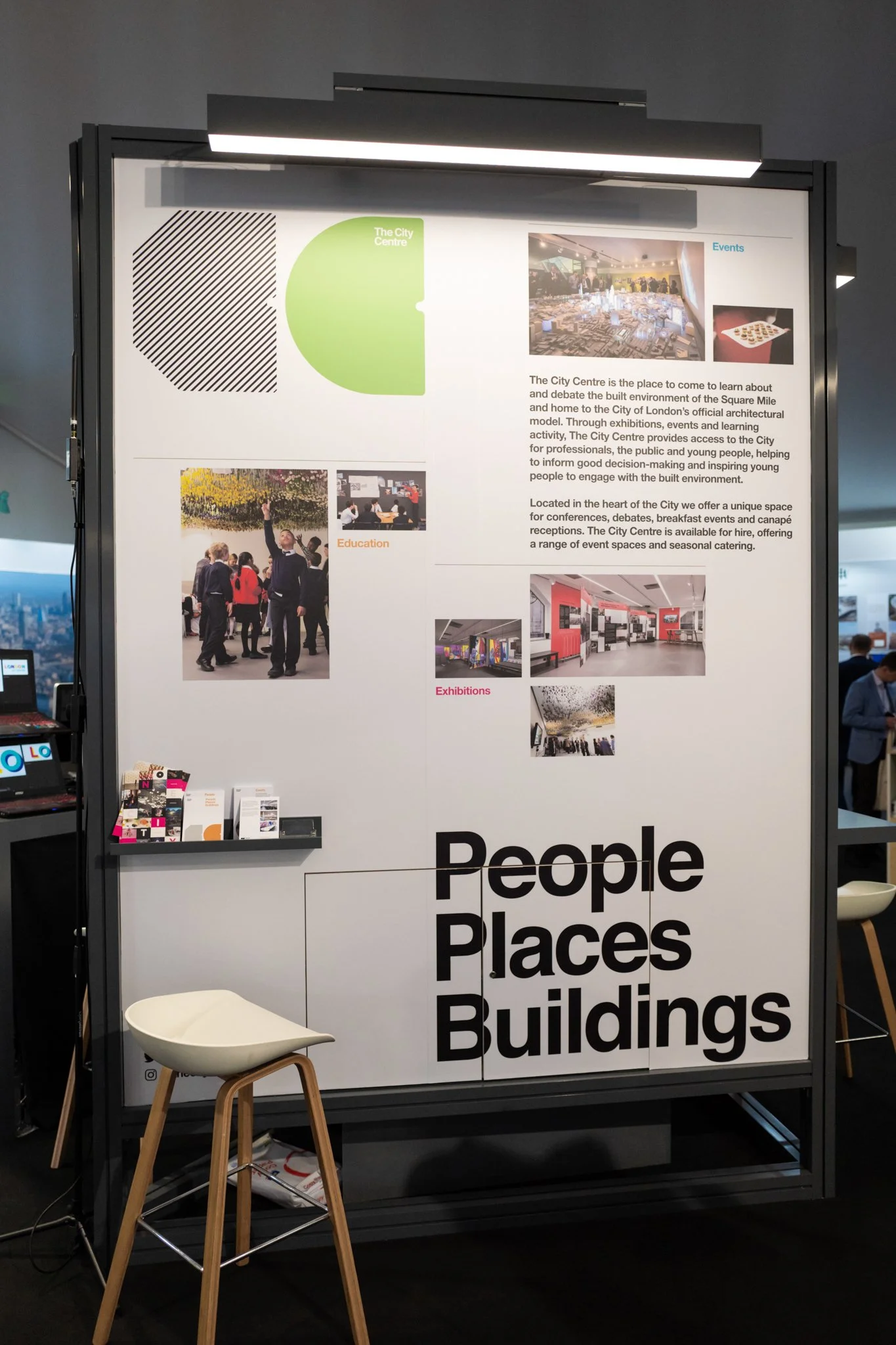 An informational display board about The City Centre, with sections on Events, Education, and Exhibitions, along with pictures of people at the venue and interior design. The lower part features bold text saying "People Places Buildings." A white cha
