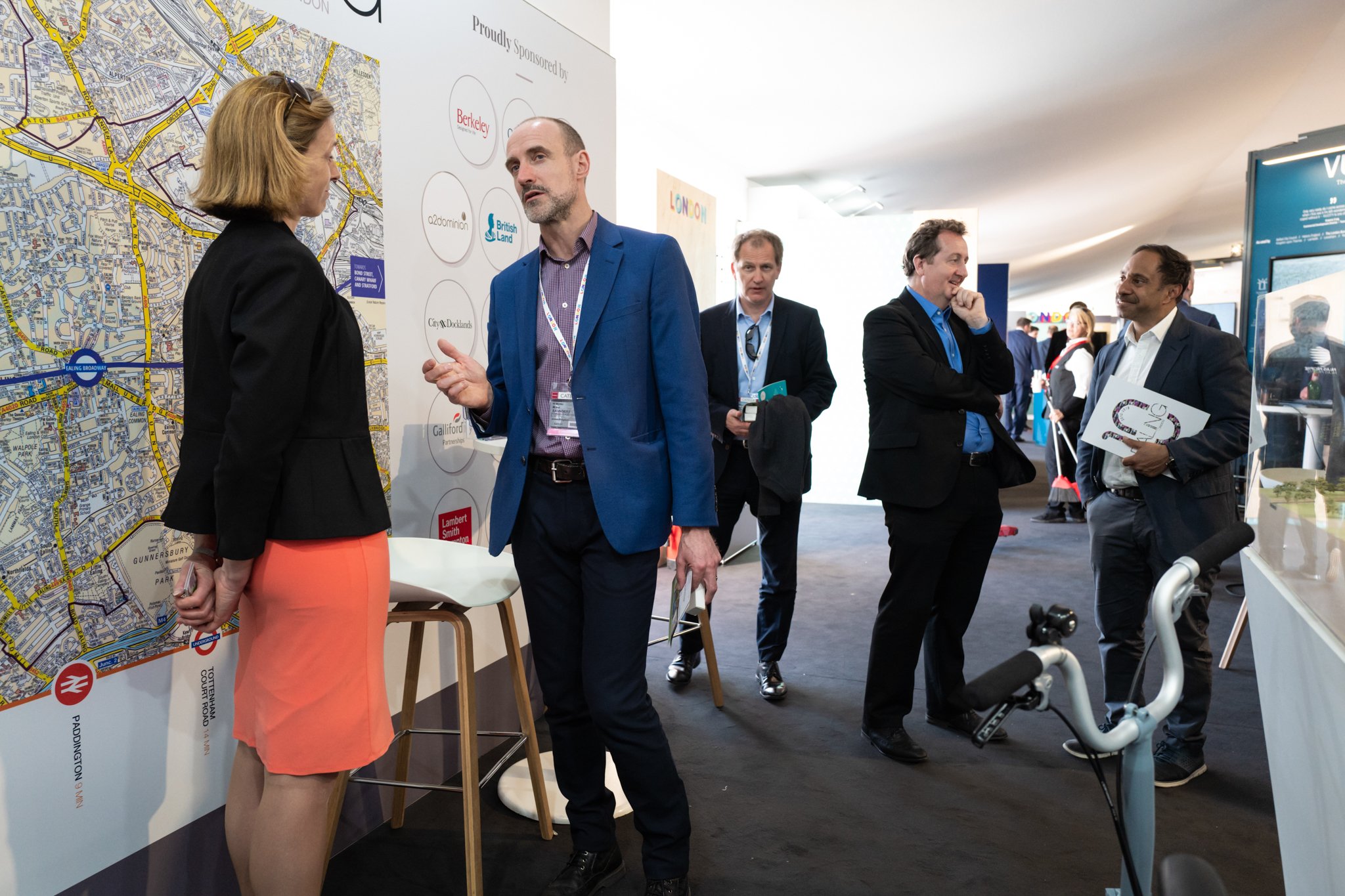 Group of professionals at a conference, engaging in conversation near a large map of London on the wall.