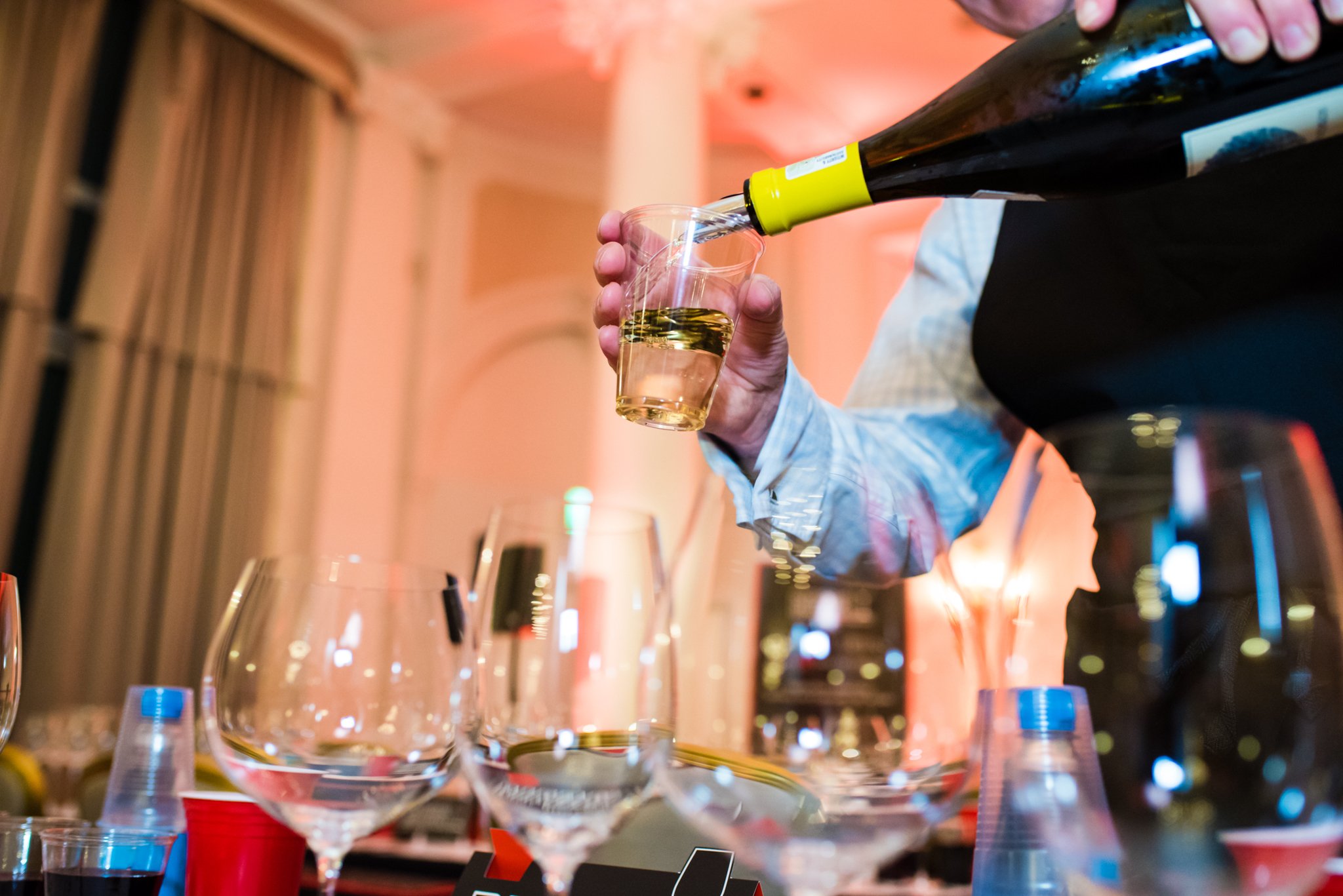 Person pouring white wine from a bottle into a wine glass at a social gathering or event.