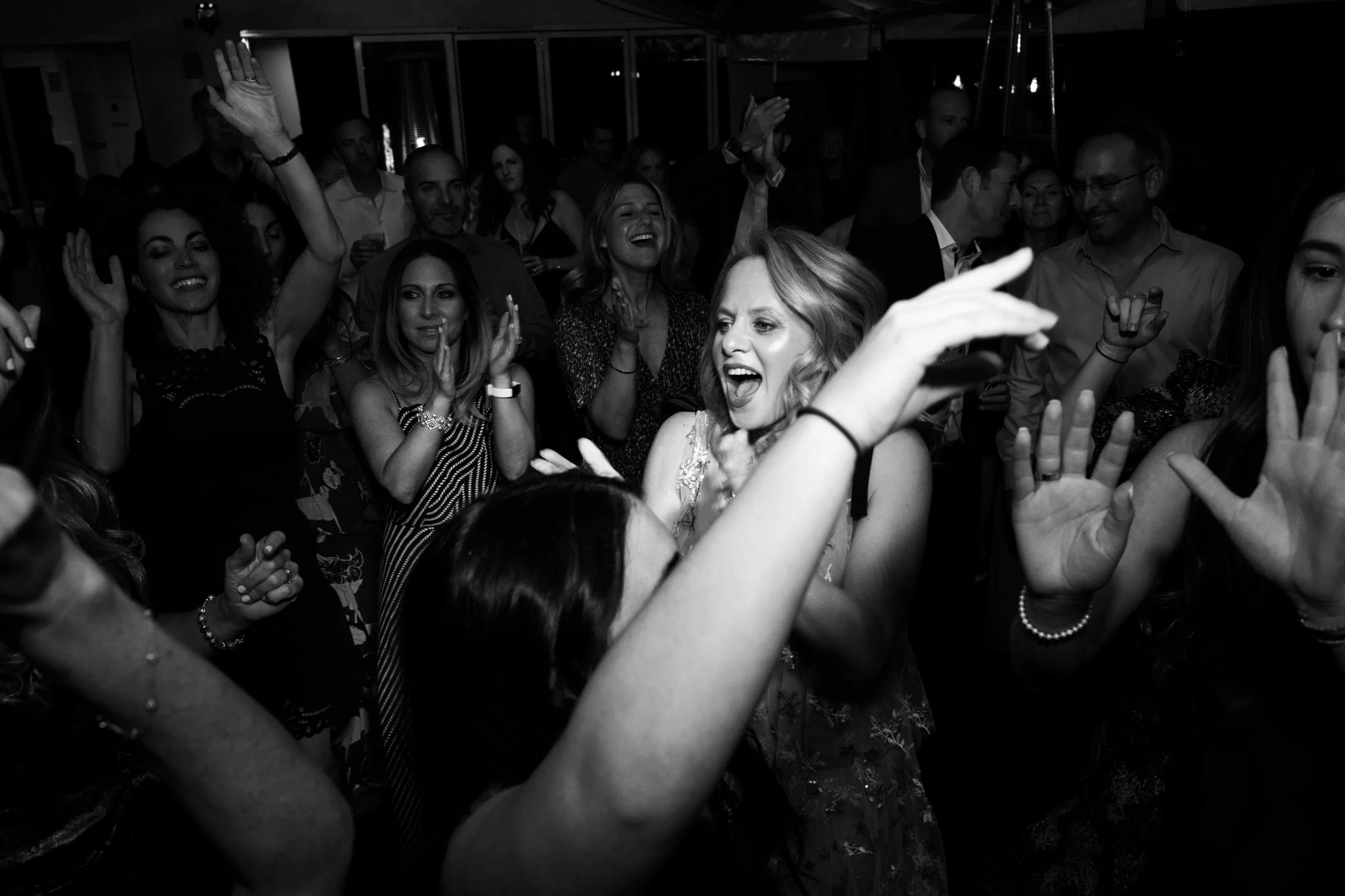 A group of people dancing and celebrating at a party, some with hands raised, smiling and laughing in a lively social gathering.