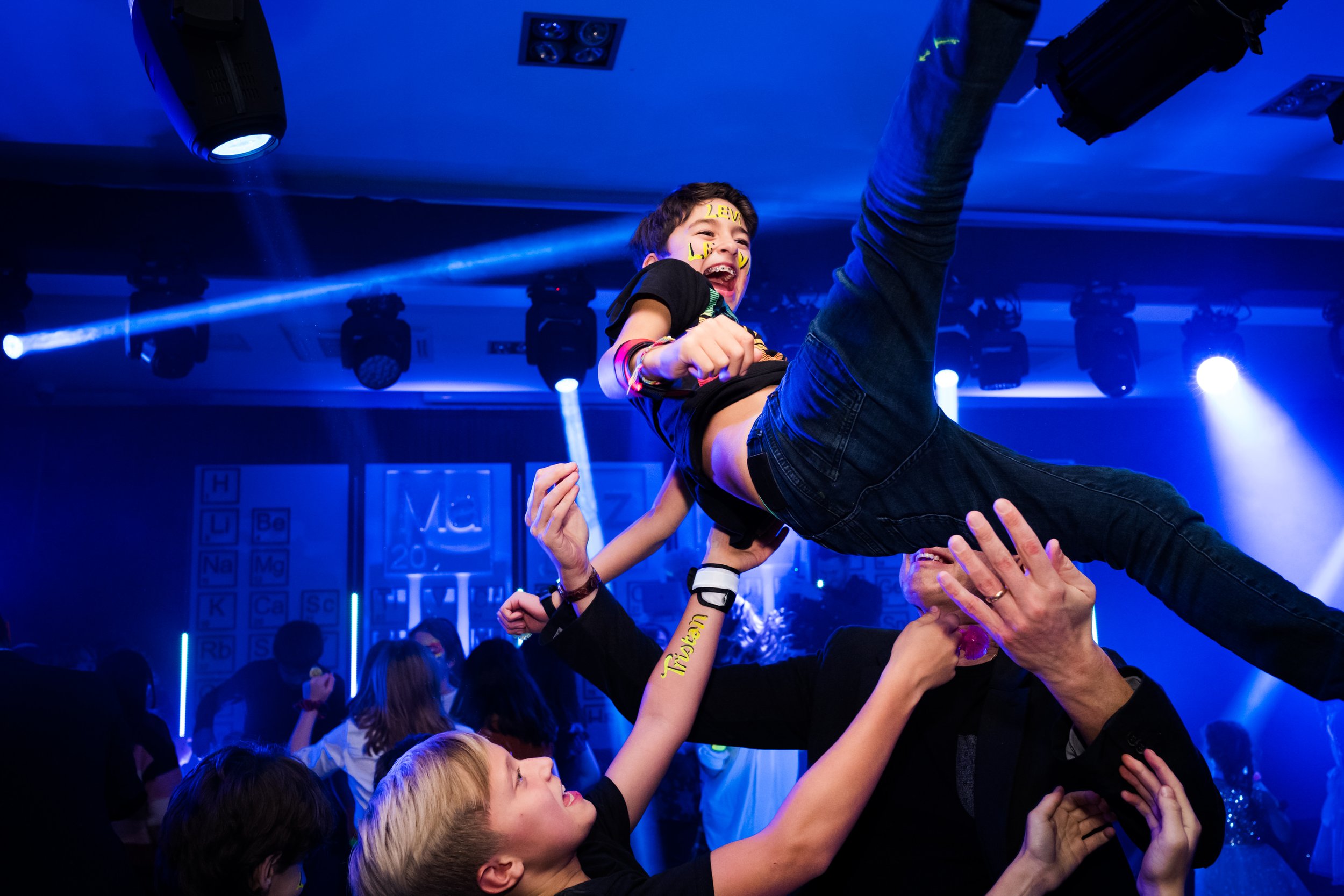 Young person being lifted in the air at a dance party with blue lighting and energetic atmosphere