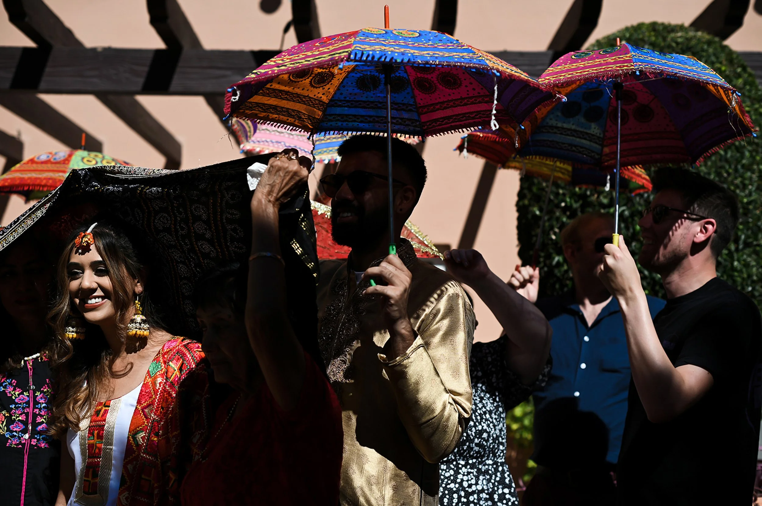 People celebrating outdoors with colorful umbrellas, some wearing traditional Indian attire.