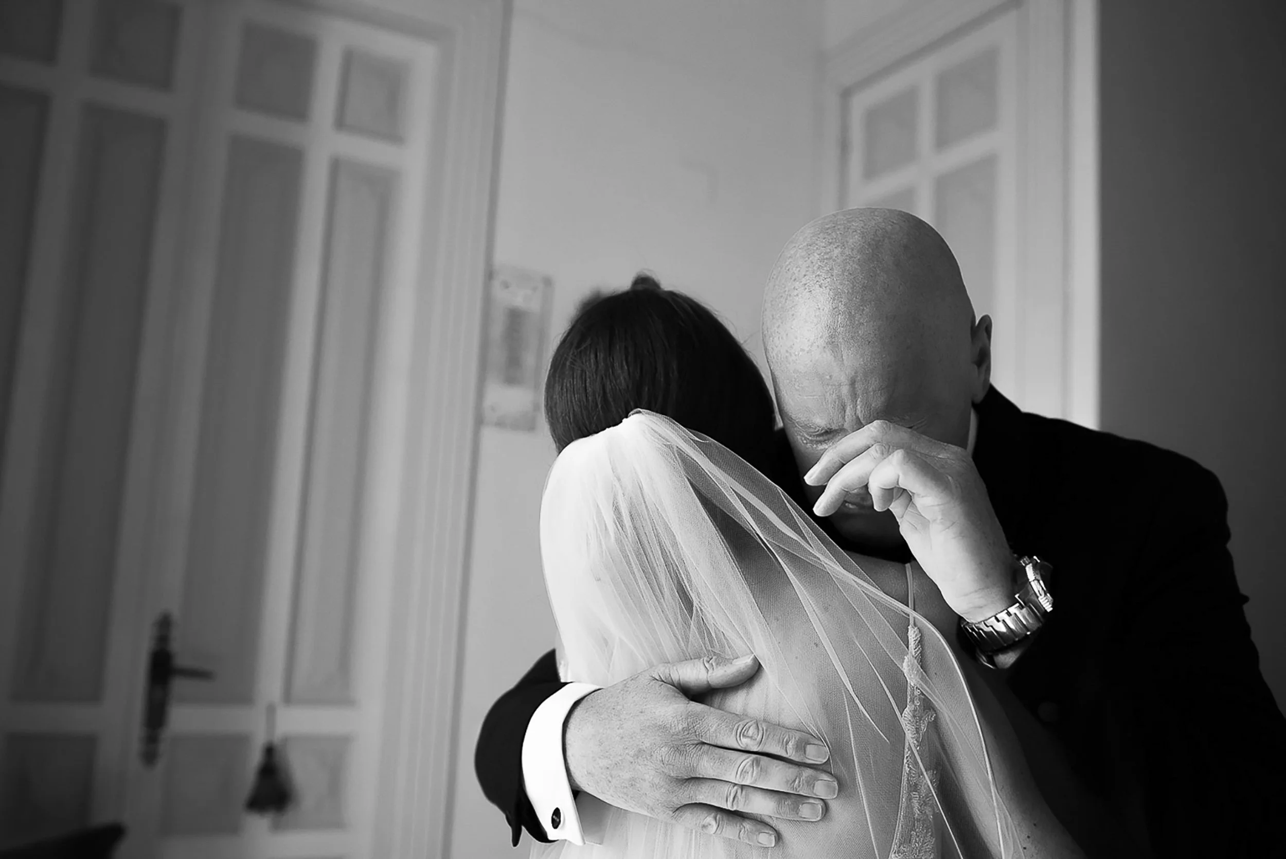 An emotional embrace between a bride and a man, possibly her father, on her wedding day in black and white.