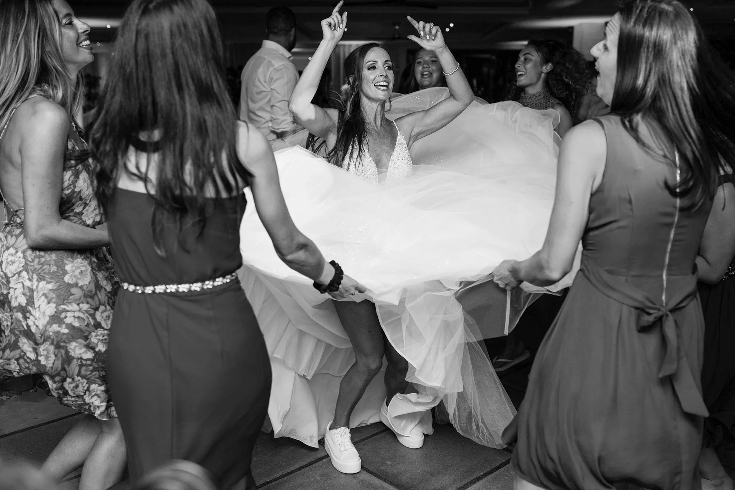 A bride dancing in a wedding dress surrounded by friends during her wedding celebration.