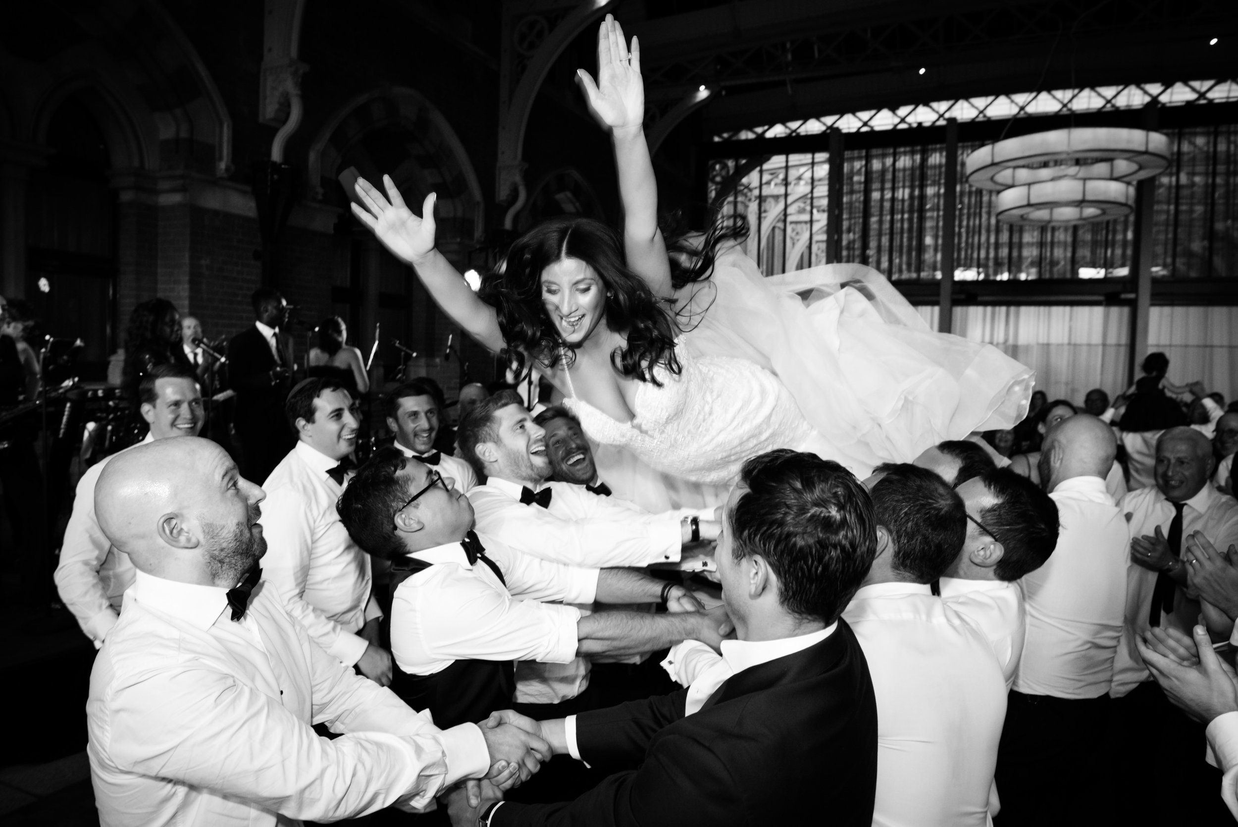A bride being lifted by a group of men during a celebration at a wedding reception.