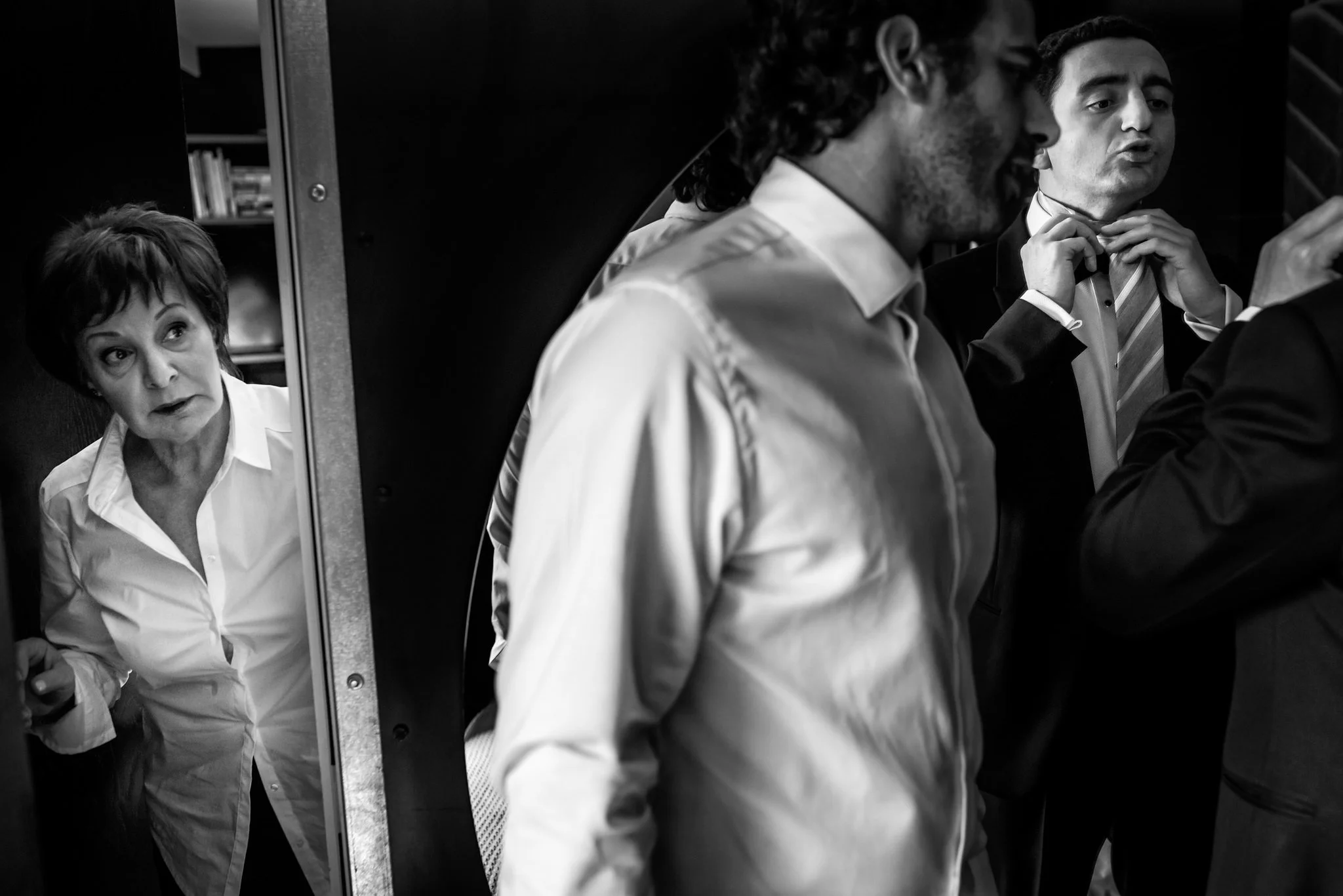 A group of people, including a woman and three men, dressing toliing up for a formal event in a closet or dressing room.