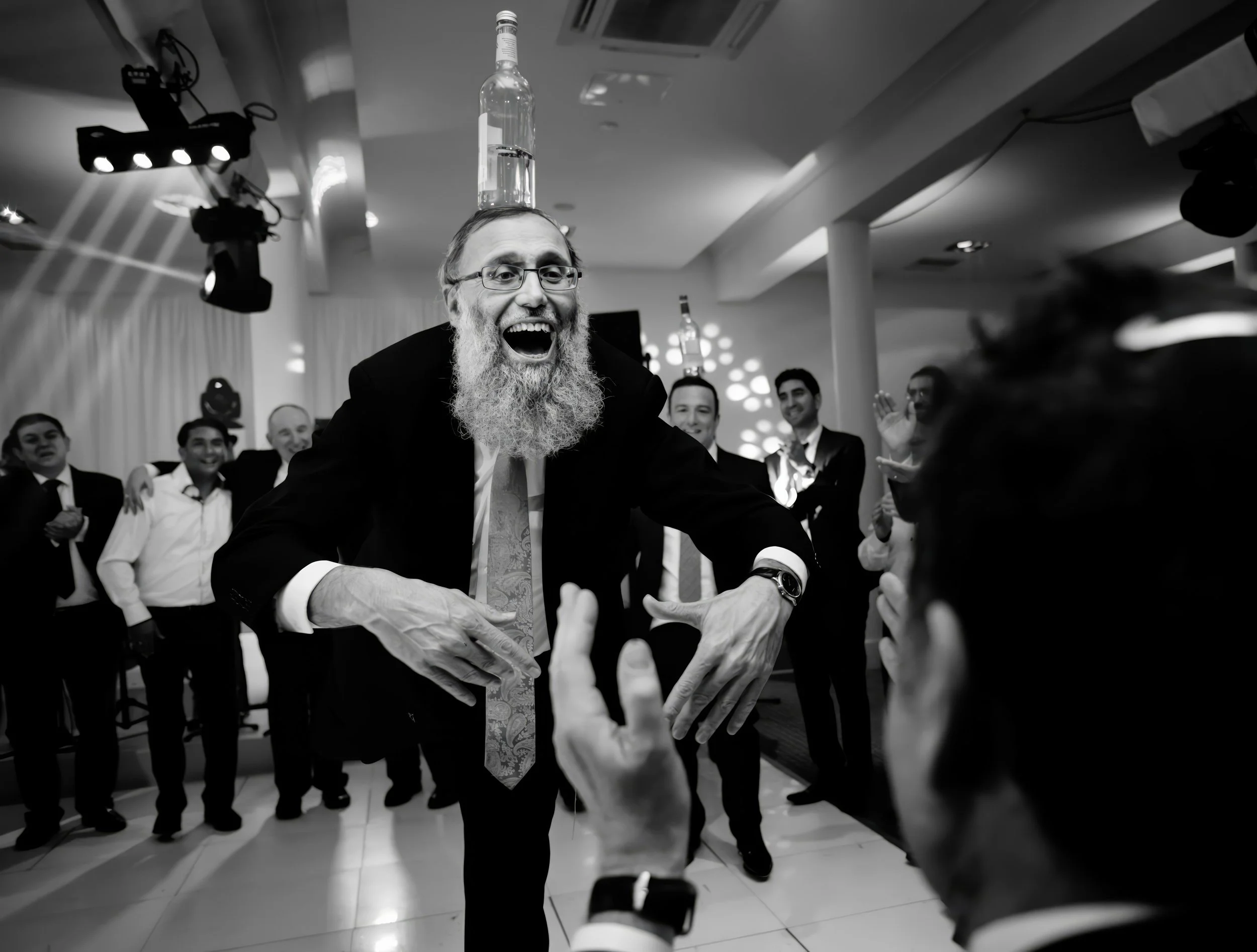 A man with a long beard balancing a bottle of water on his head at a lively party with several people clapping and smiling in the background.
