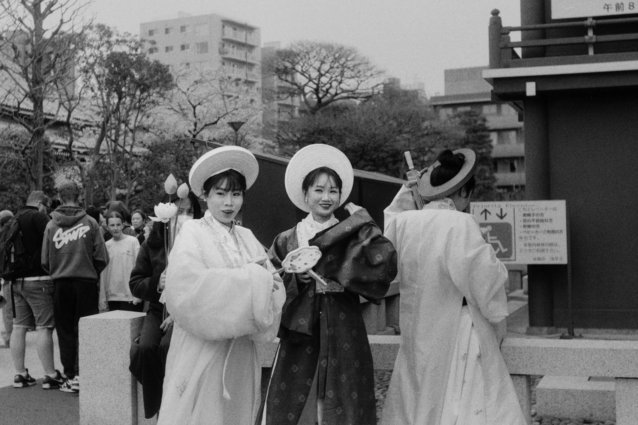 Group of women dressed in traditional Korean hanbok at an outdoor event, with people and buildings in the background.