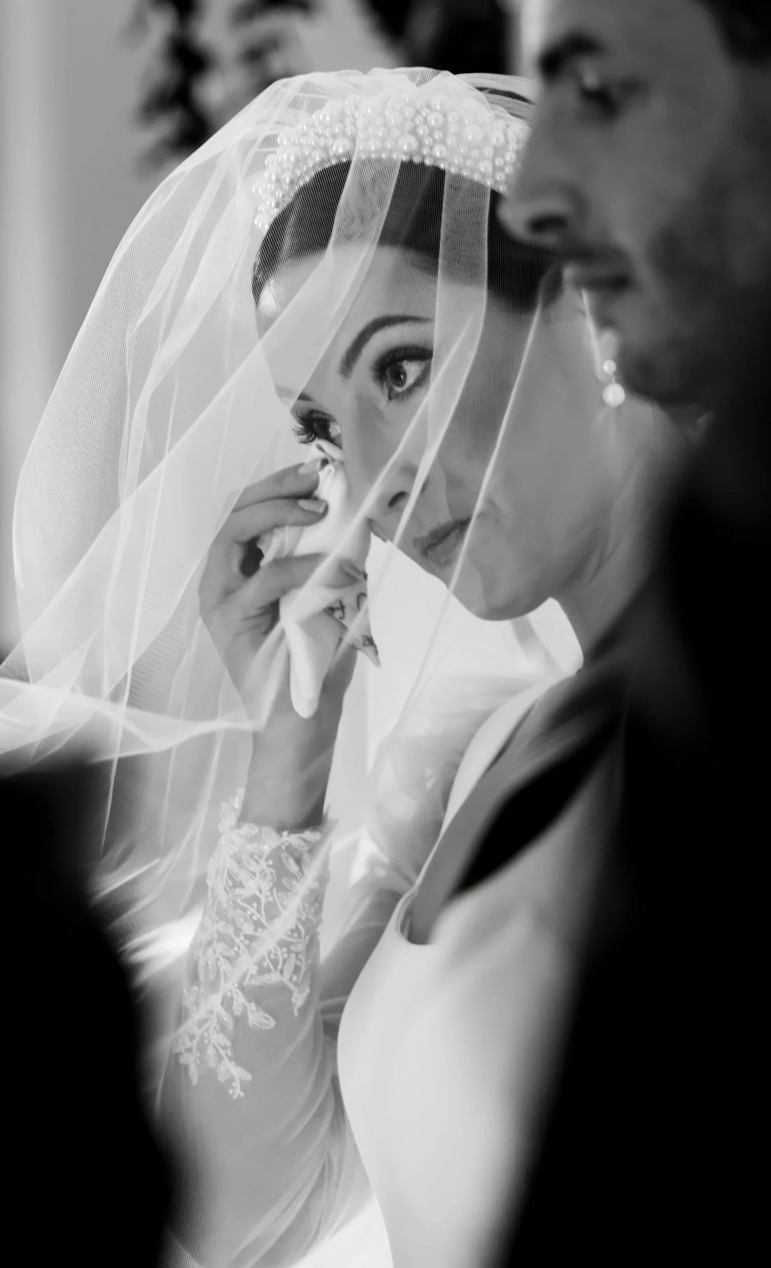 A bride with a veil and lace wedding dress tears up during a wedding ceremony, with a groom beside her.