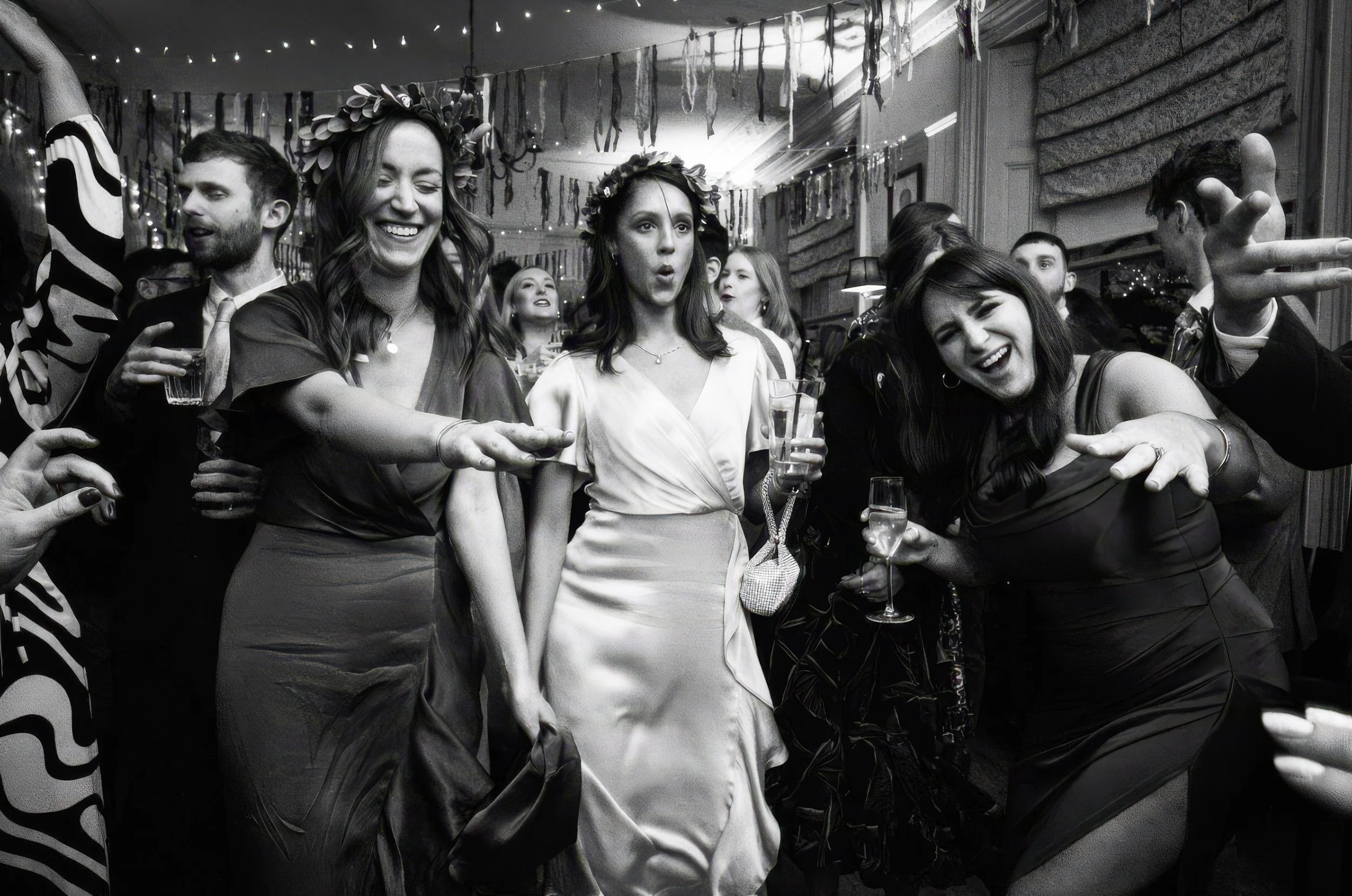 People dancing and enjoying themselves at a party with decorations and string lights, some holding drinks.