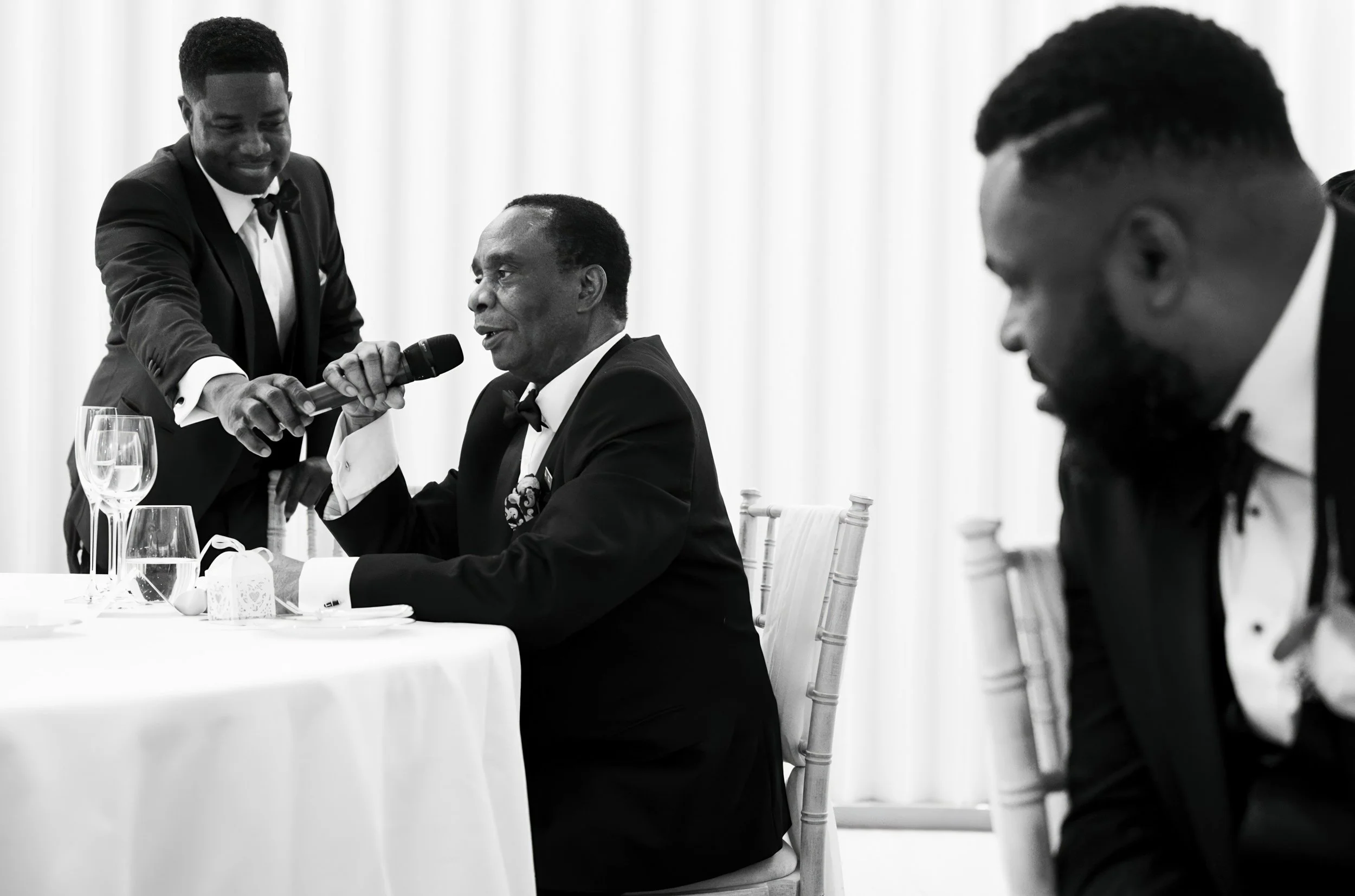 Man in tuxedo speaking into microphone held by another man in tuxedo at a formal event