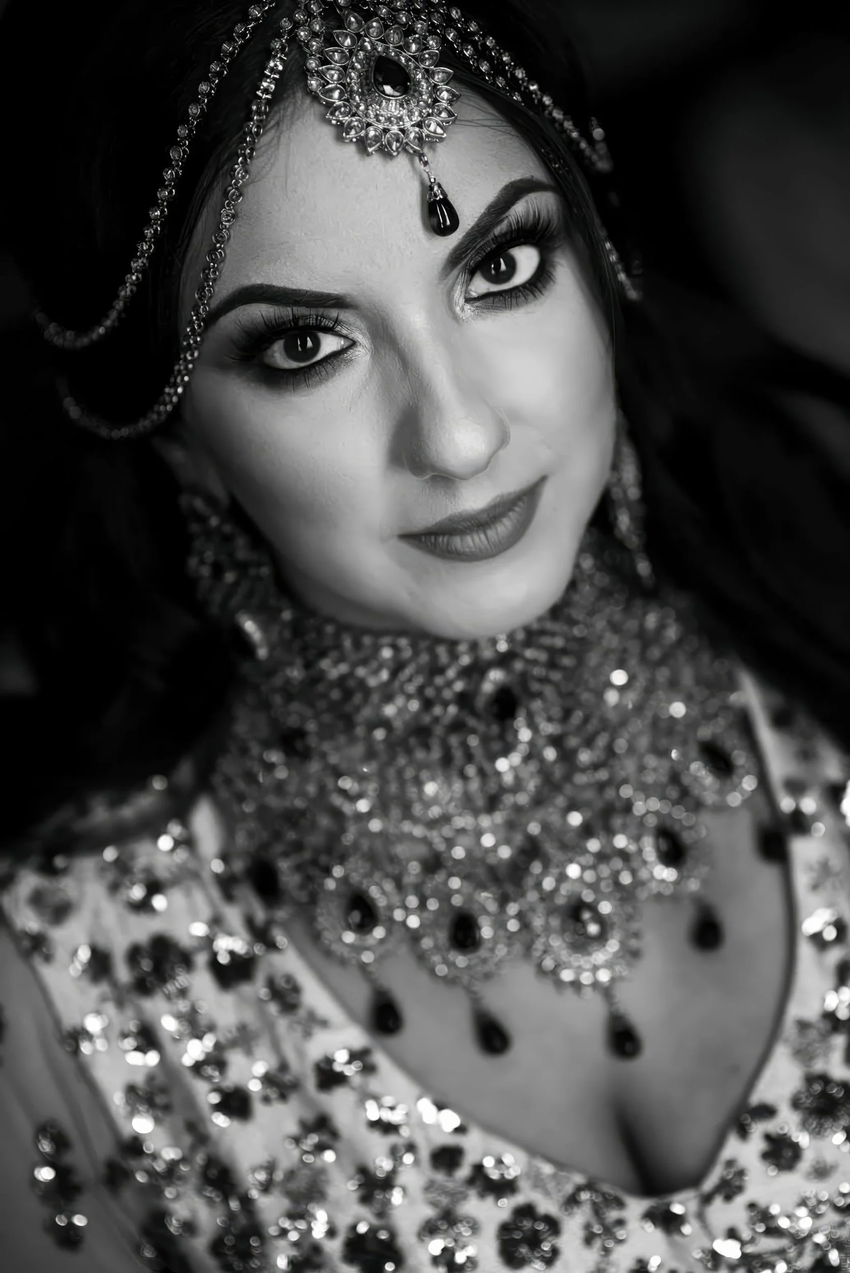 A woman dressed in traditional Indian attire with intricate jewelry, including a headpiece, earrings, and a heavily embellished outfit.