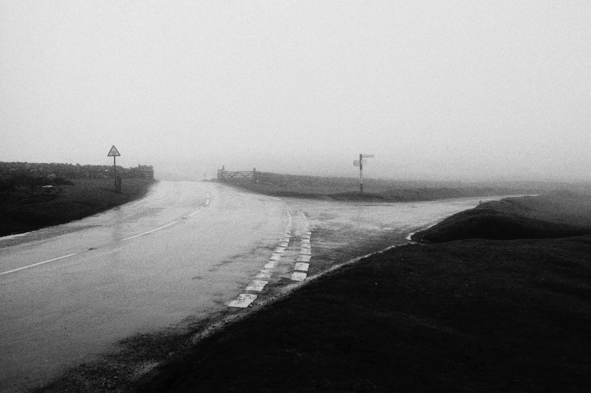 A foggy, deserted rural road with road signs and a partially fogged background.