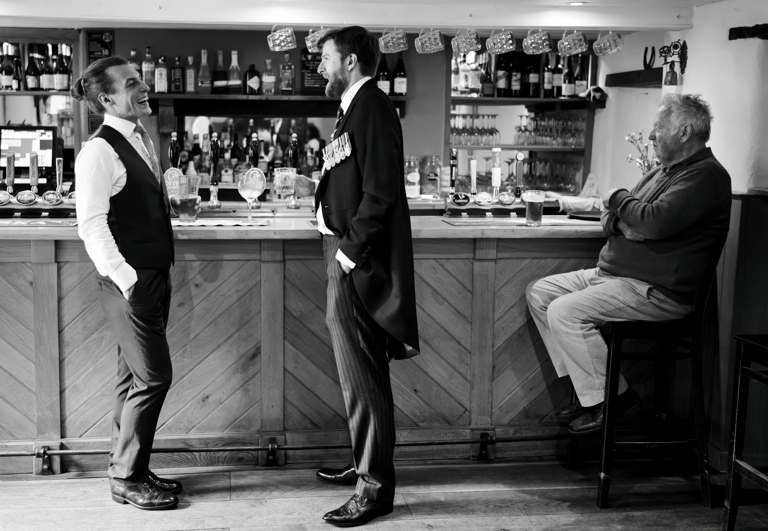 Two men in formal attire and a bartender are engaged in a conversation at a bar. The man on the left is smiling with his hands in his pockets, while the man on the right is speaking and wearing medals. An older man is sitting on a high stool at the b