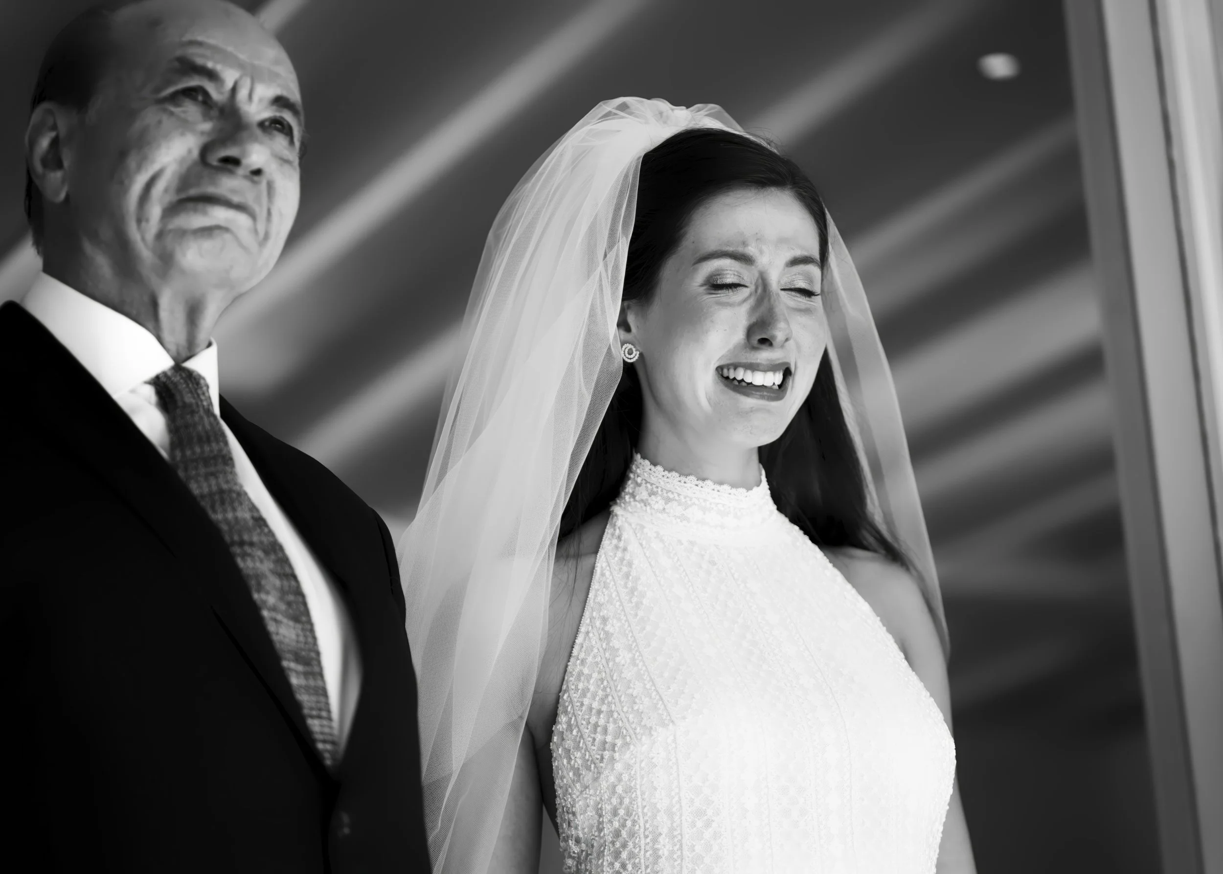 A bride with closed eyes and a distressed expression standing next to a man, likely her father, during a wedding. The bride is wearing a wedding dress and veil, and the man is wearing a dark suit with a tie.
