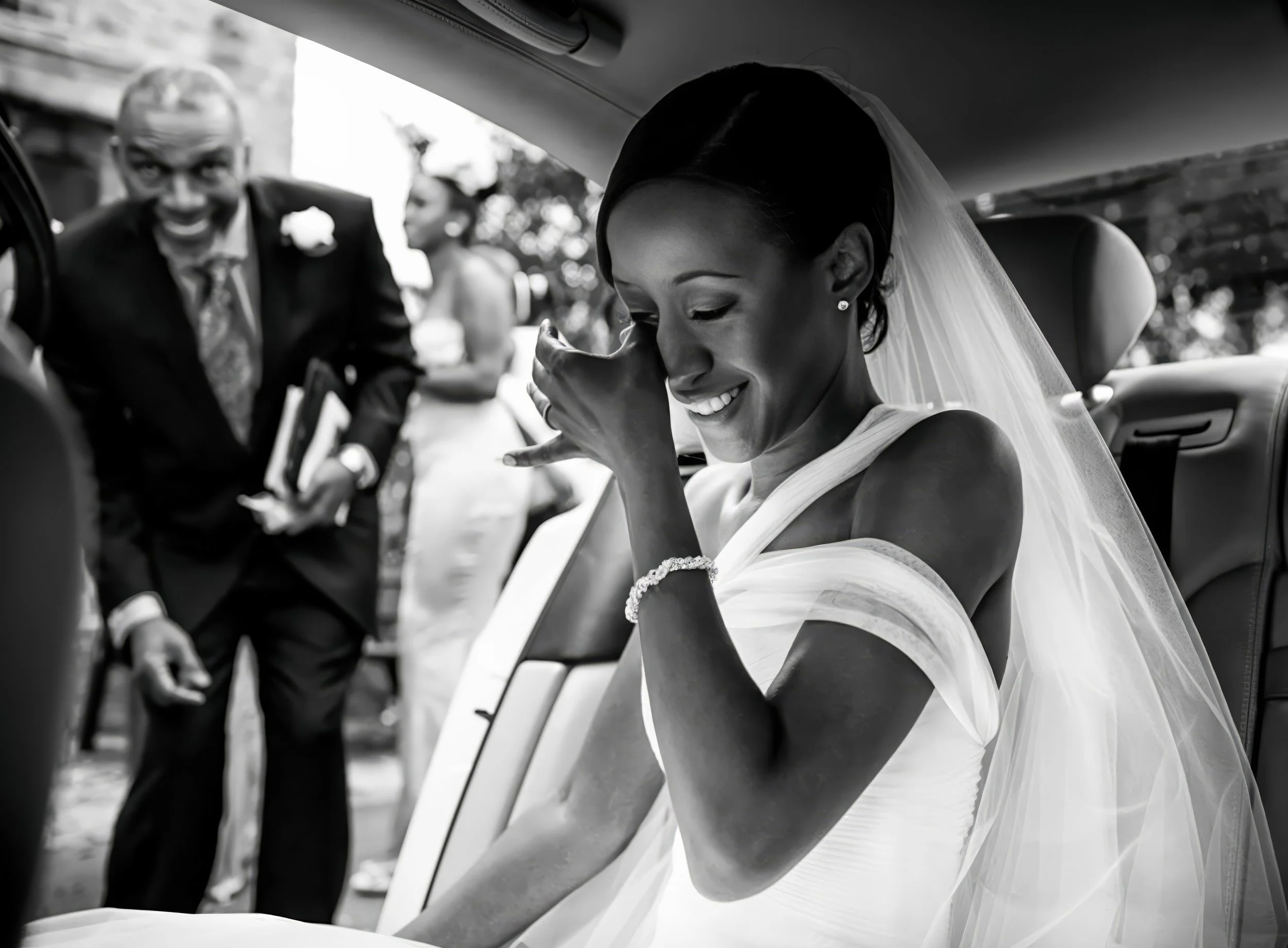 A joyful bride sitting in a car, wiping tears with a tissue, while her father and another woman stand outside, celebrating at her wedding.