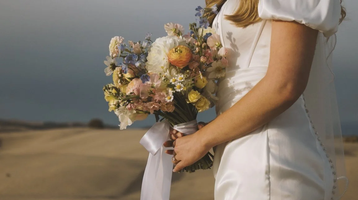 Bride holding colorful bouquet with ribbon in a desert landscape.