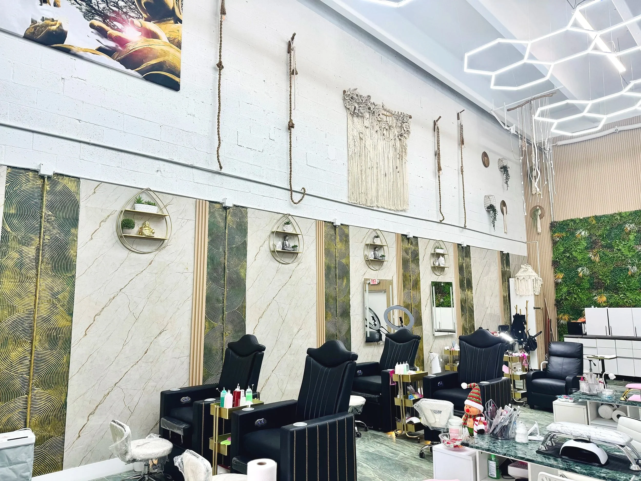 Interior of Kathy's Excellent Spa with black reclining chairs, shelves with small decorative items, mirrors, and a green living wall on the right side. Ceiling has geometric light fixtures and hanging decorations.