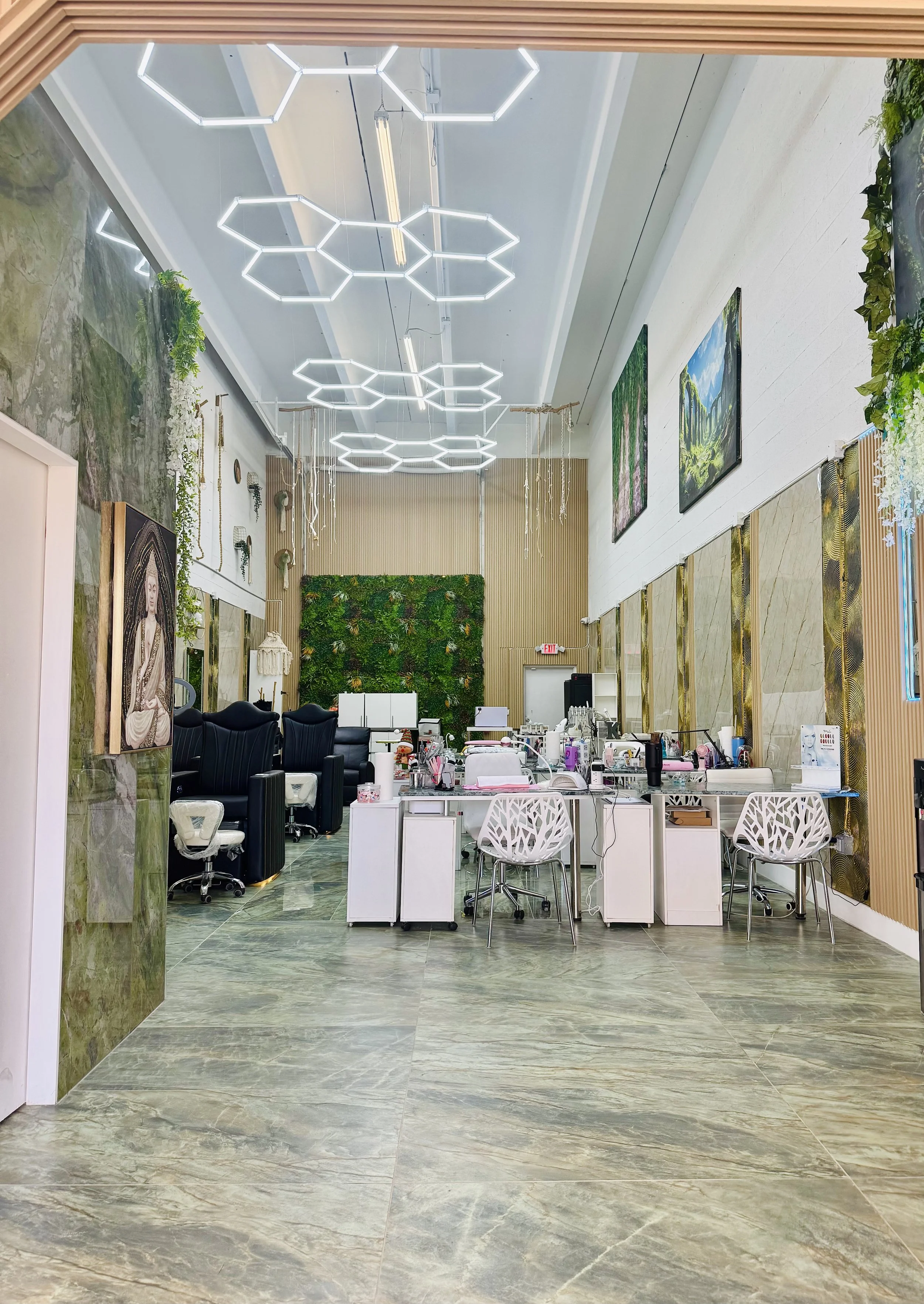 Interior of a modern salon or spa with manicure stations, ergonomic chairs, and decorative artwork including landscape paintings and a green wall.