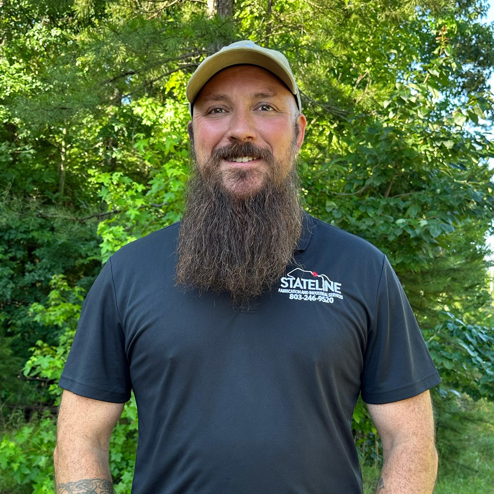 Alex Bucca, owner of Stateline Fabrication, standing in front of green trees smiling and wearing a black polo