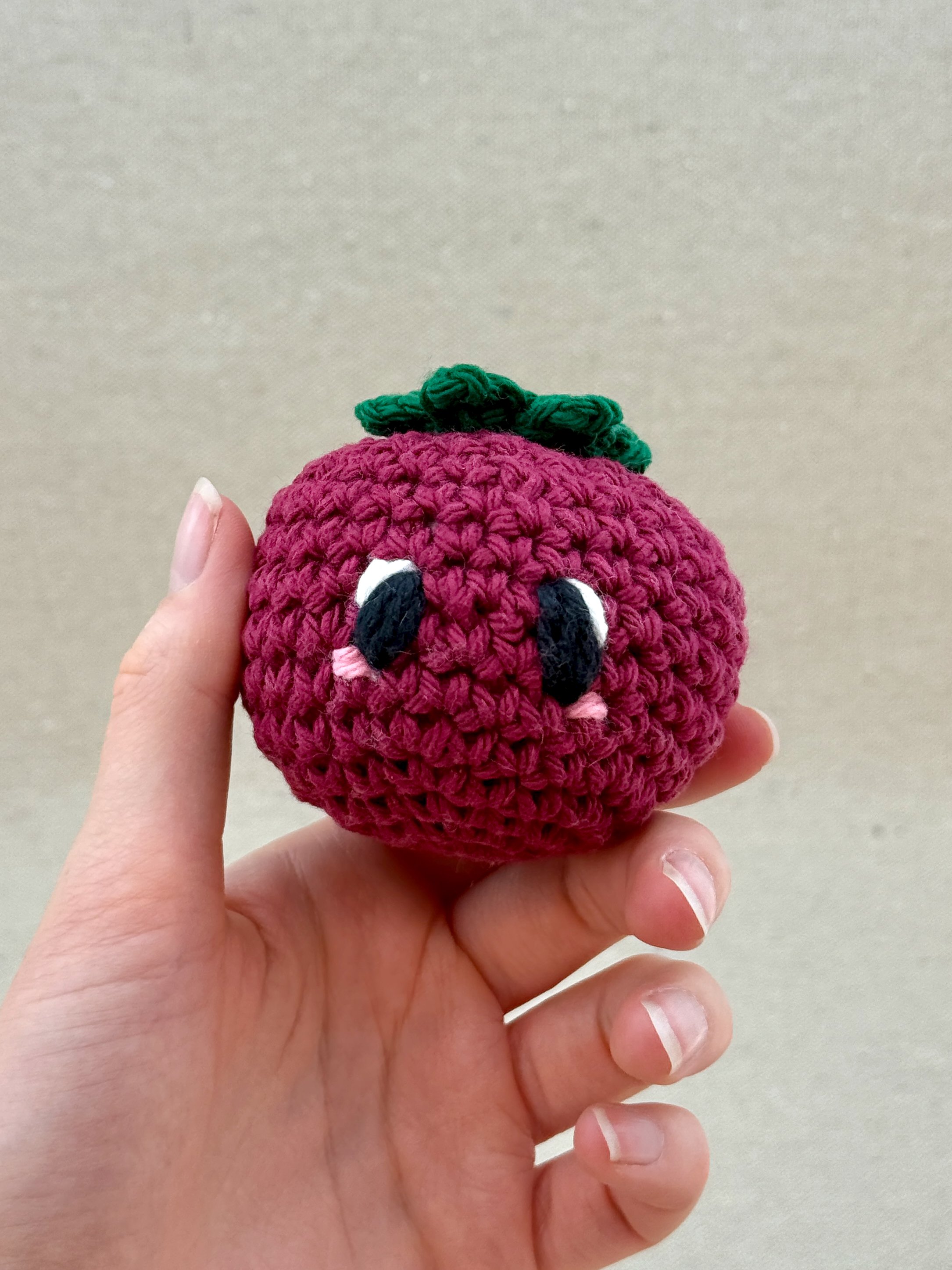 A burgundy crochet tomato plush held in a hand (Copy)