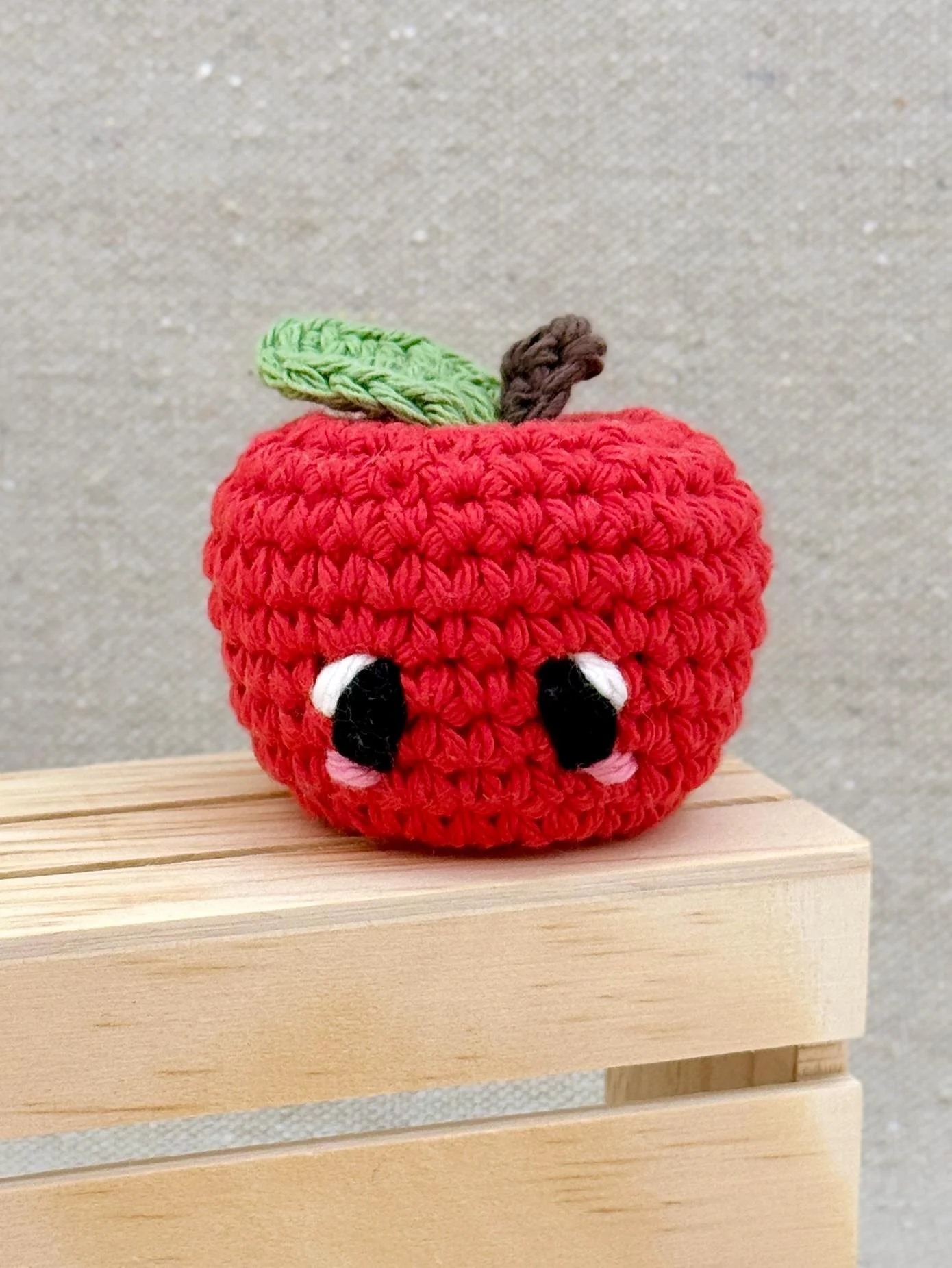A red amigurumi apple plush posed with a mini wooden crate