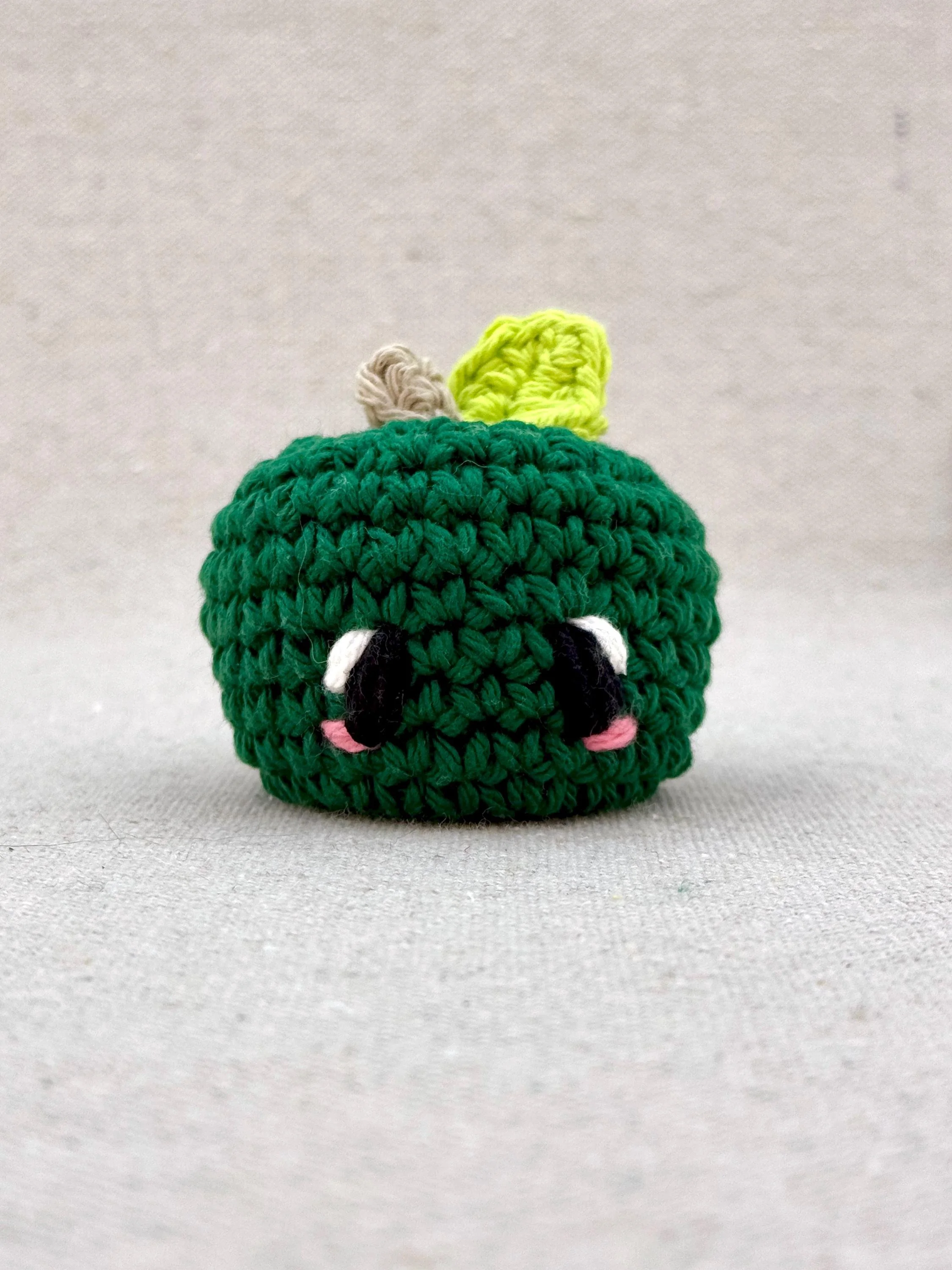 Close up of a pine green apple amigurumi plush made from cotton yarn and cotton stuffing