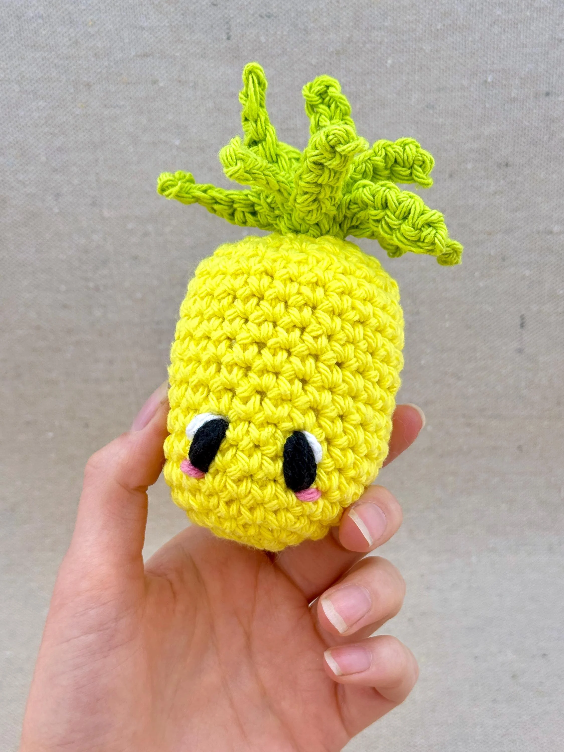 A bright yellow crochet pineapple plush held in a hand (Copy)