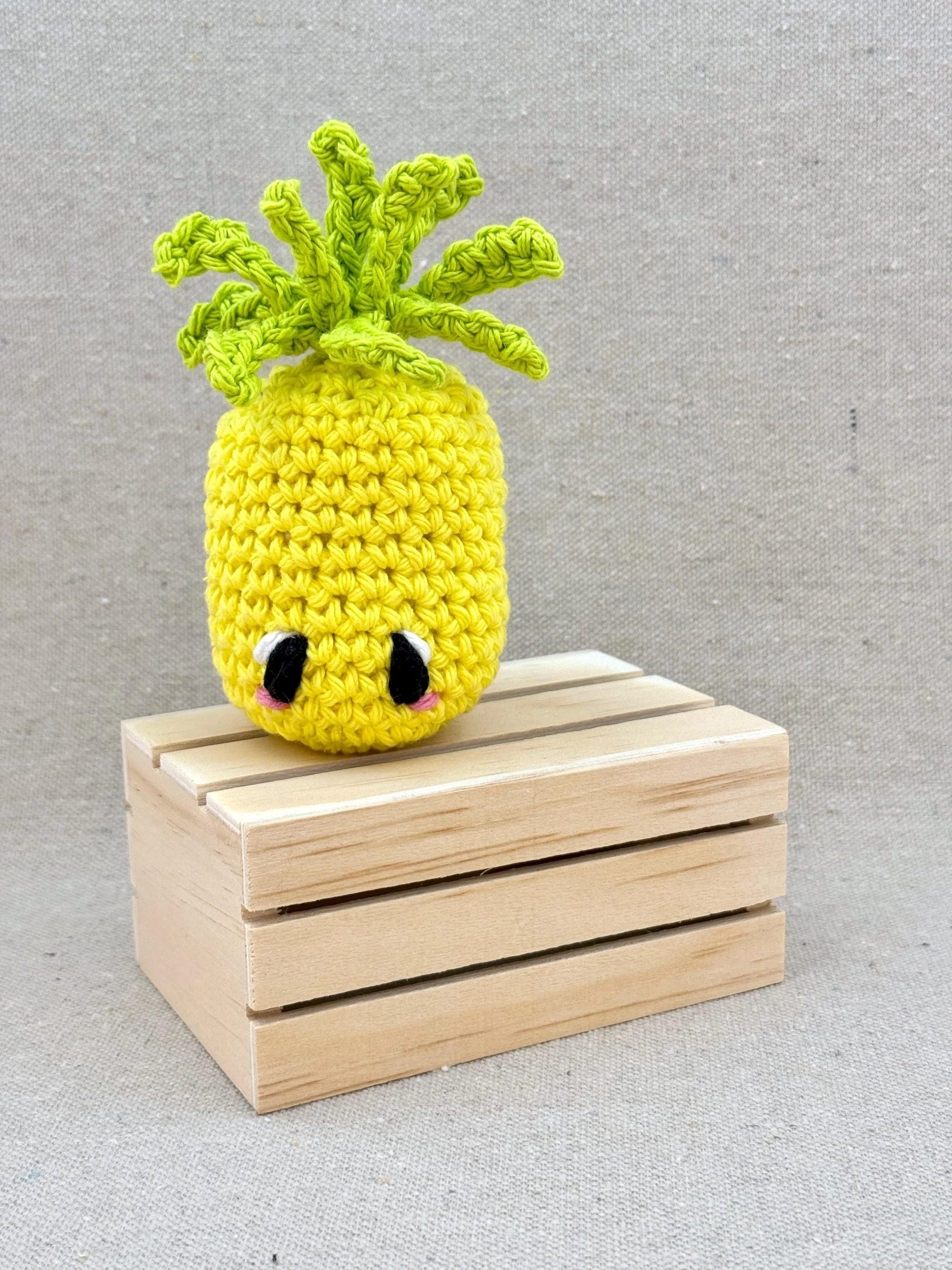 A bright yellow amigurumi pineapple plush posed with a mini wooden crate (Copy)