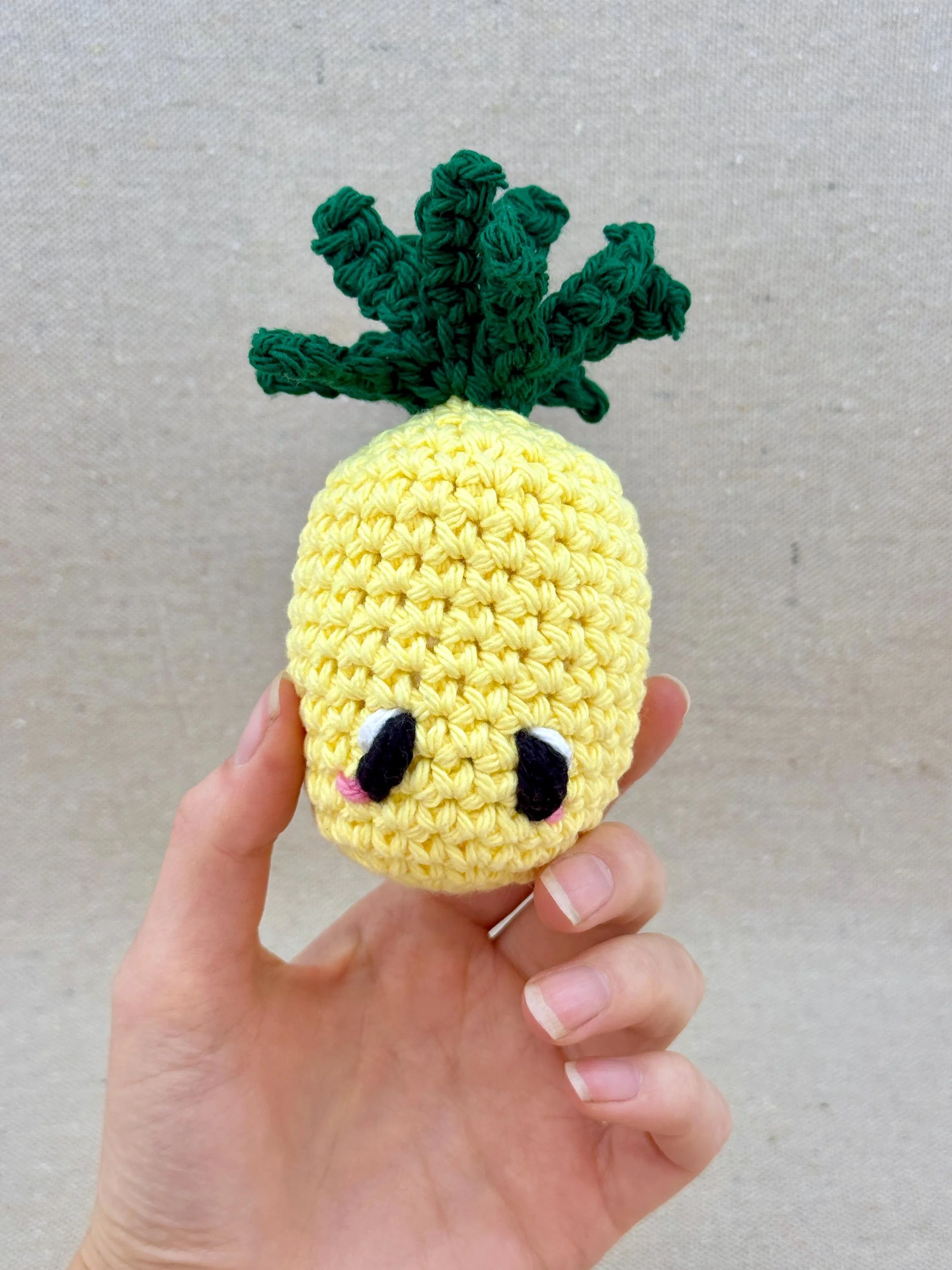 A butter yellow crochet pineapple plush held in a hand (Copy)