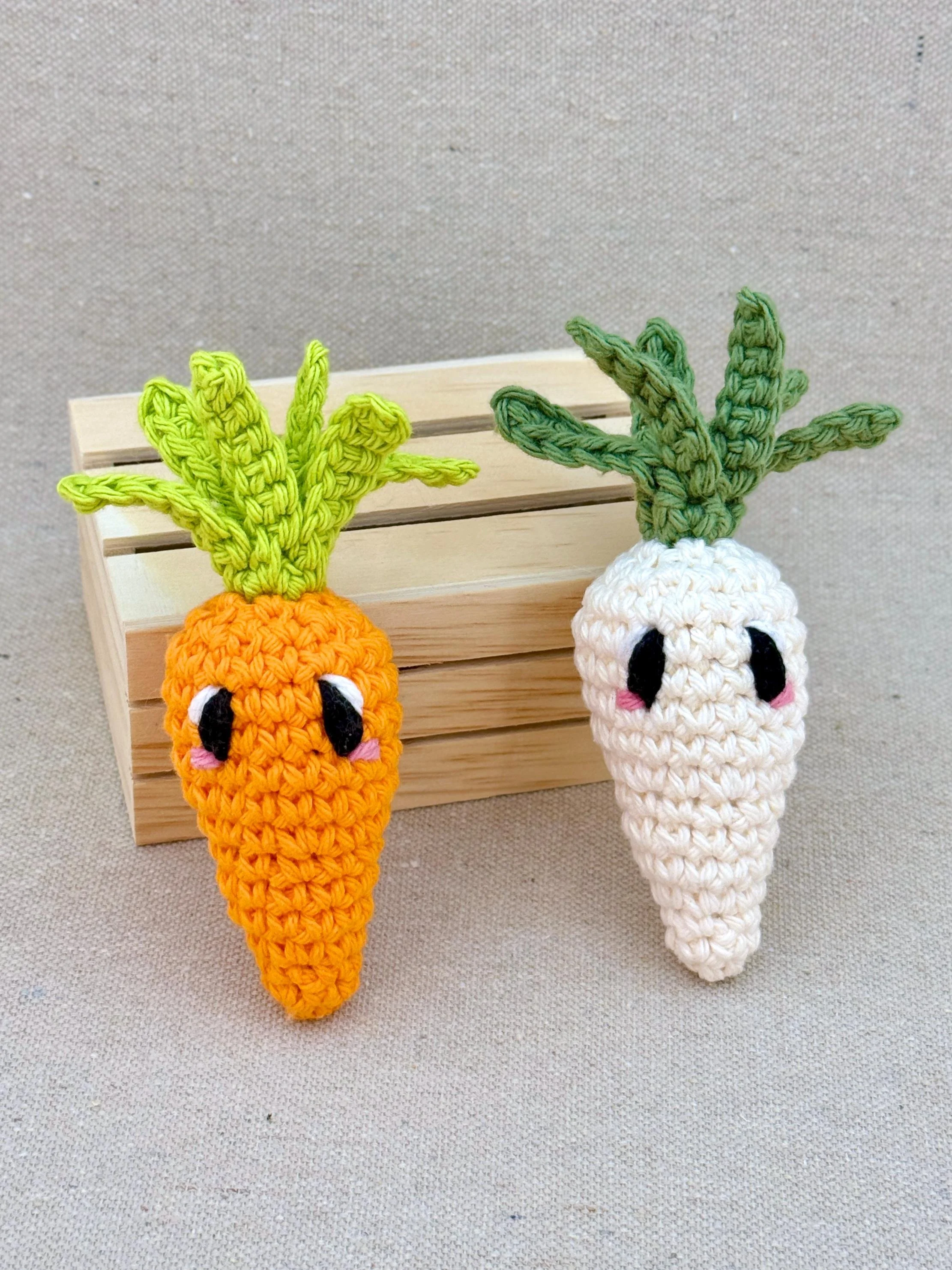 Two crochet amigurumi carrot plushies posed with a mini wooden crate in orange and cream (Copy)